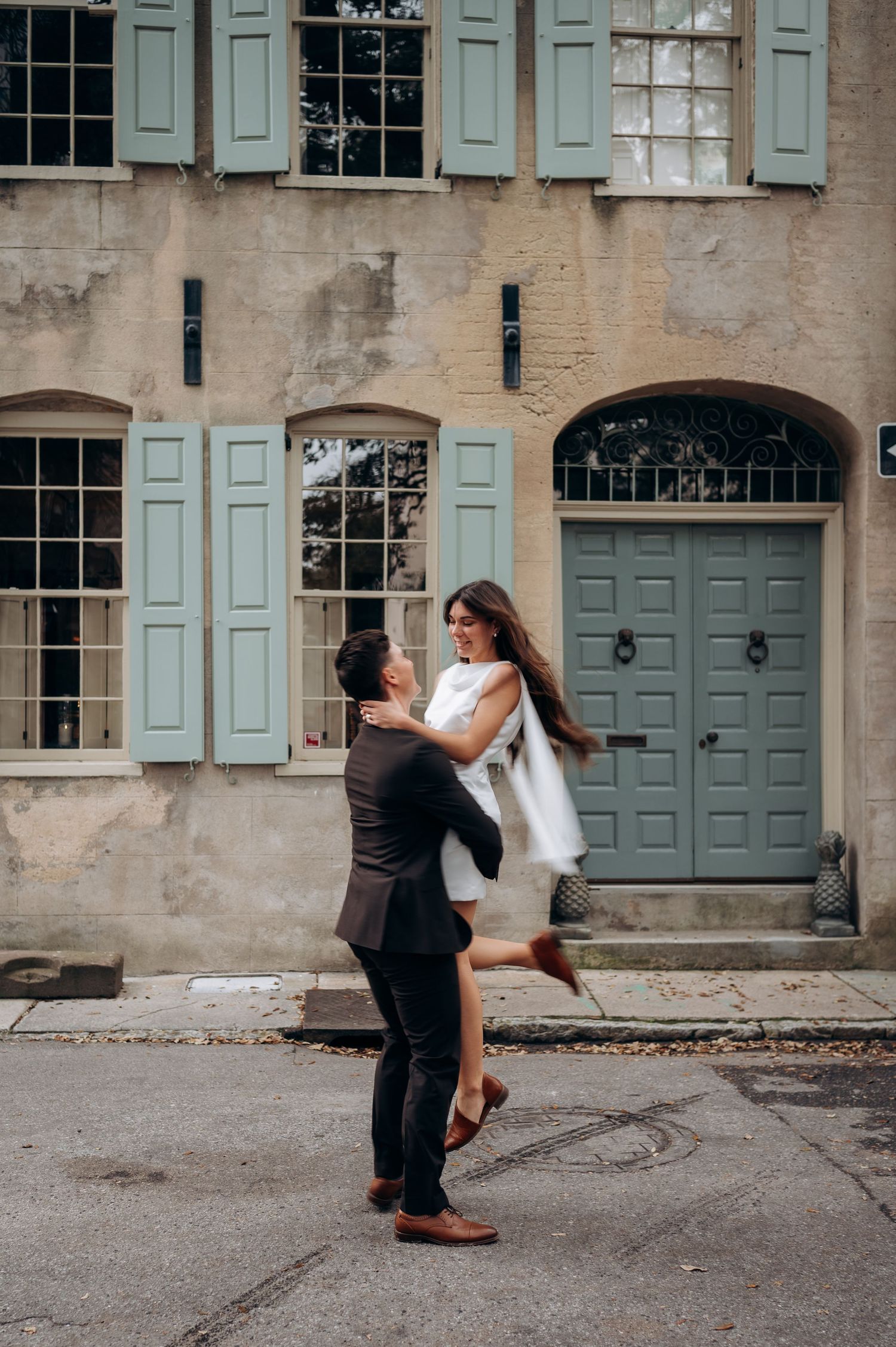 Romantic couple dancing in front of a building with teal shutters.