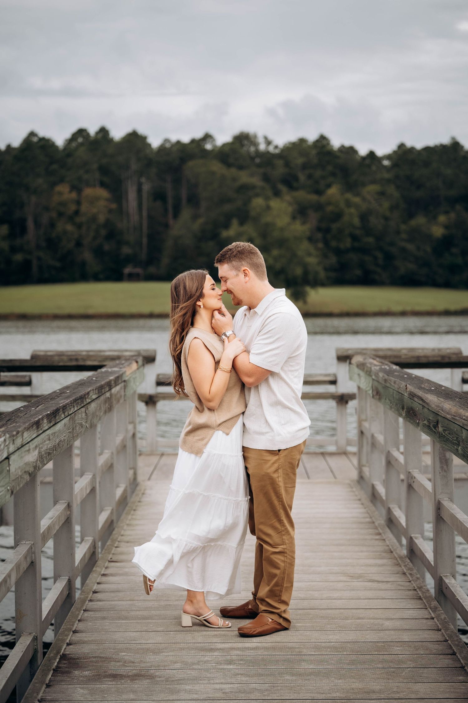 Couple in white and khaki sharing romantic moments on a wooden boardwalk over marshland.