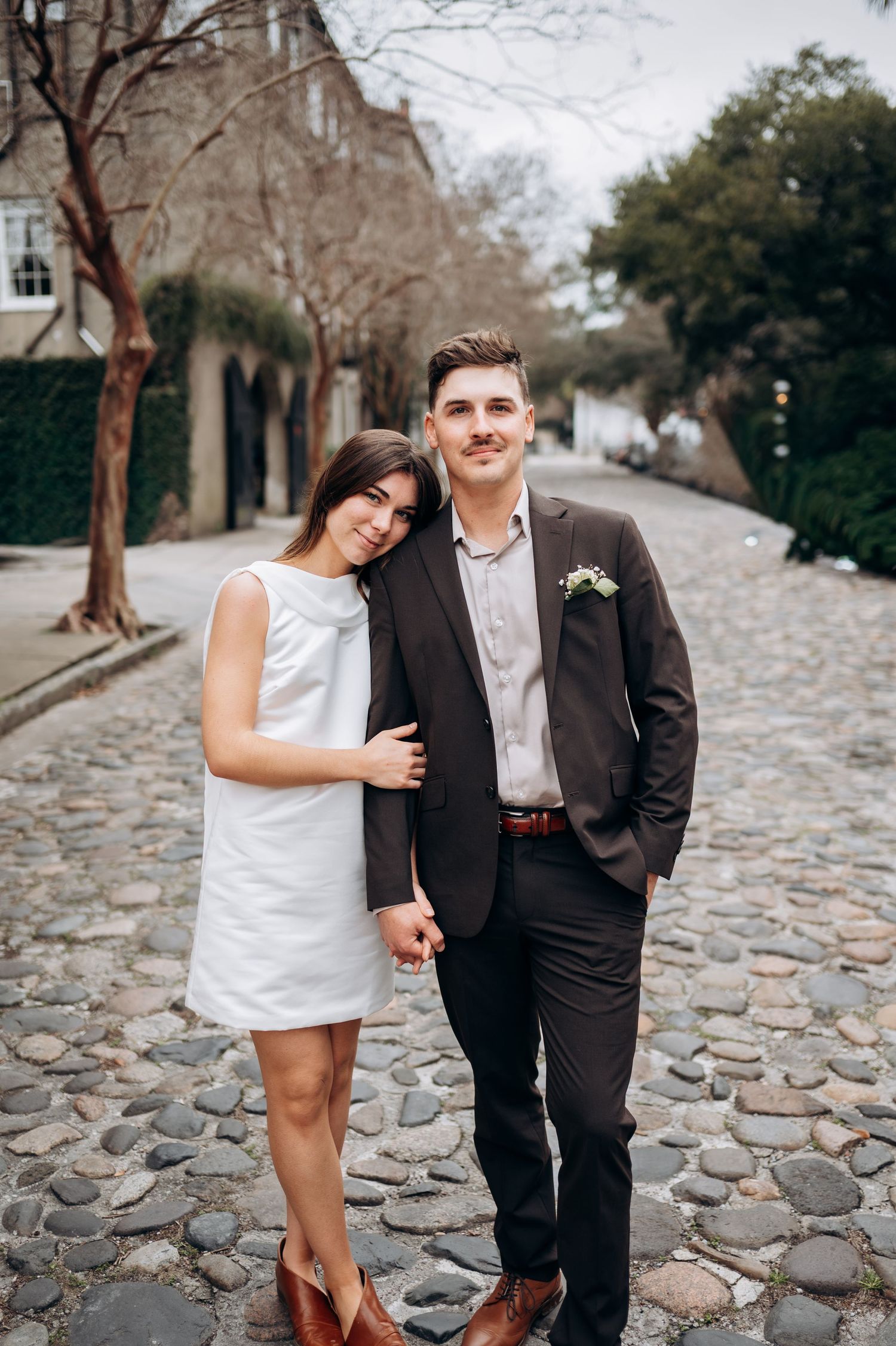 A couple poses for romantic photos on a cobblestone street with historic buildings in the background.