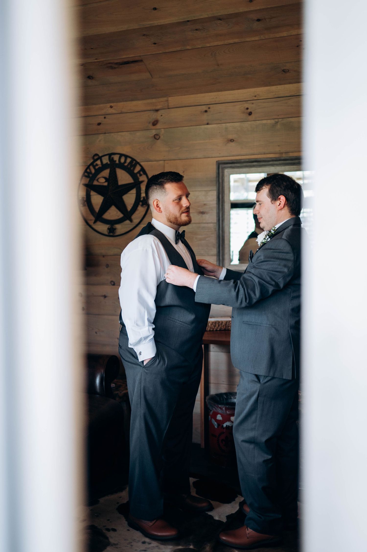 Groomsmen helping each other with formal wear preparations in a rustic wooden room.