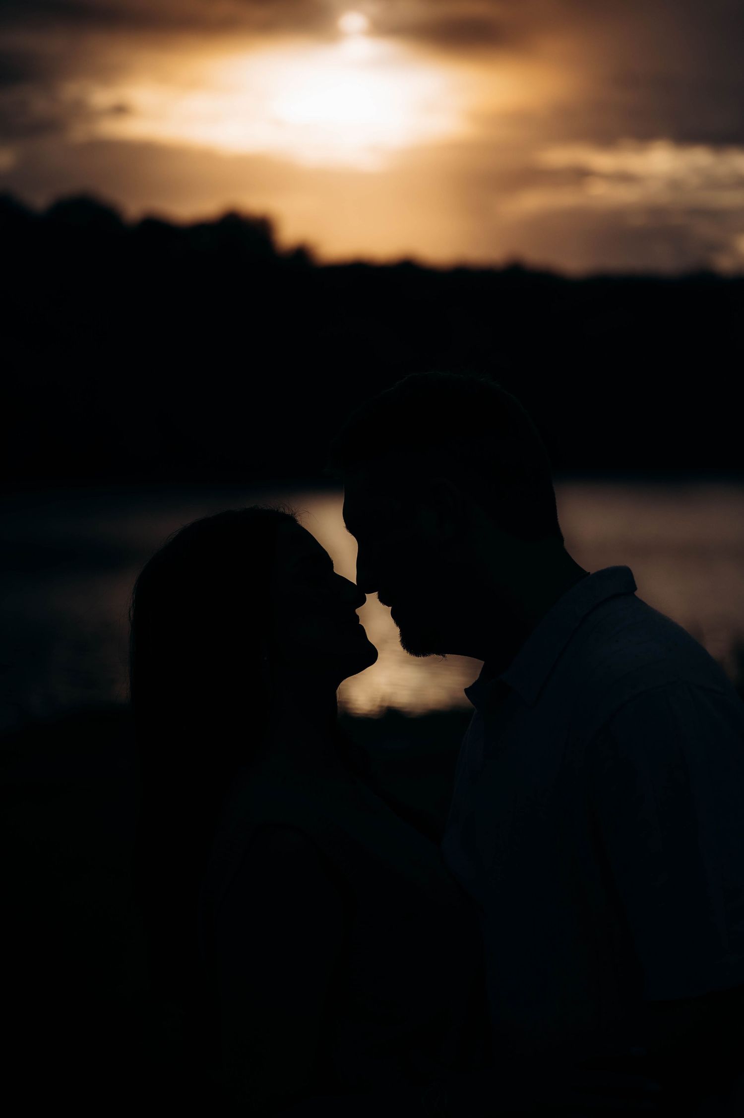 Silhouette of couple against dramatic sunset sky in romantic wedding portrait series.