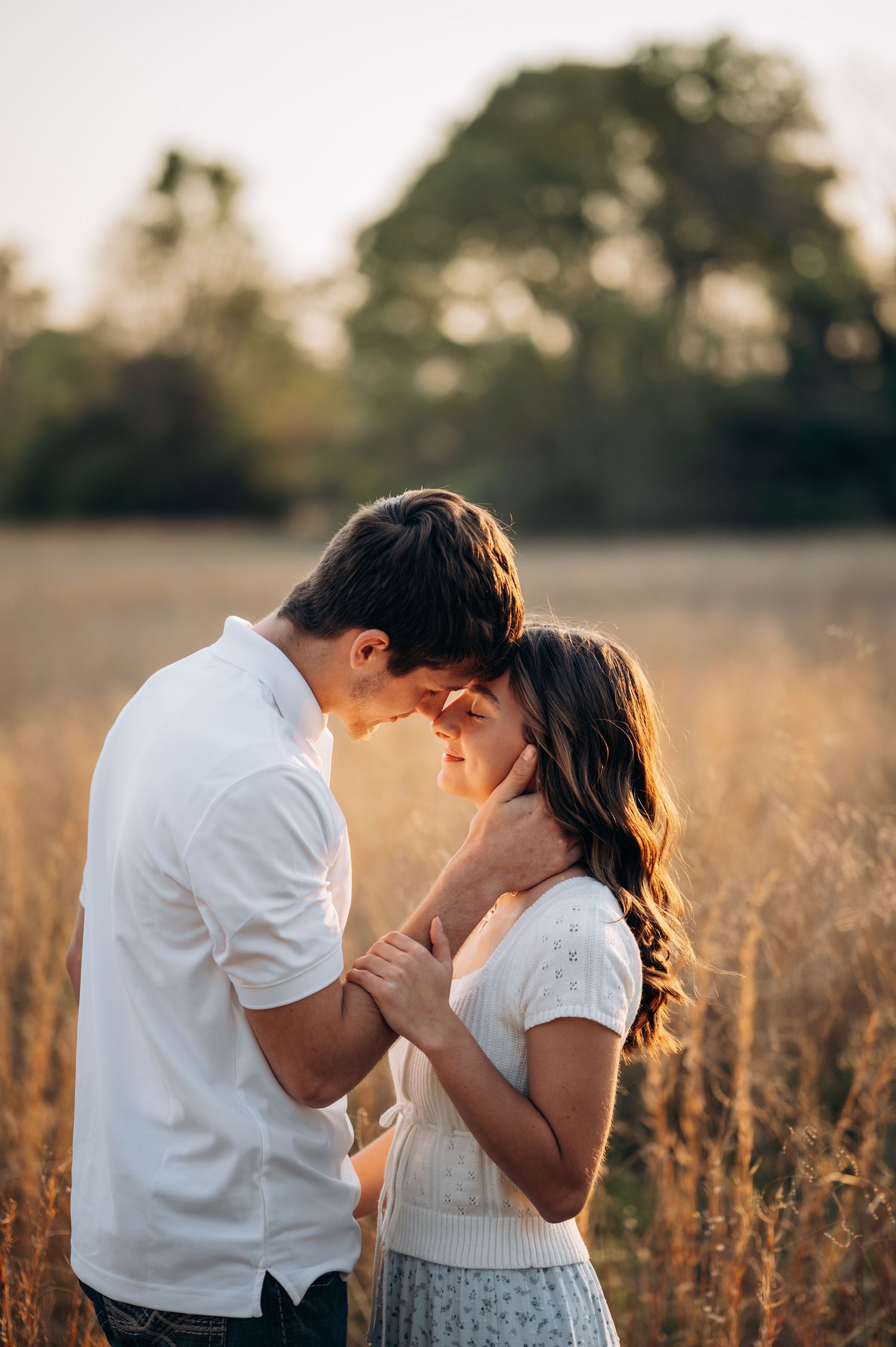 A romantic couple shares an intimate moment in a golden sunlit field, touching foreheads tenderly.