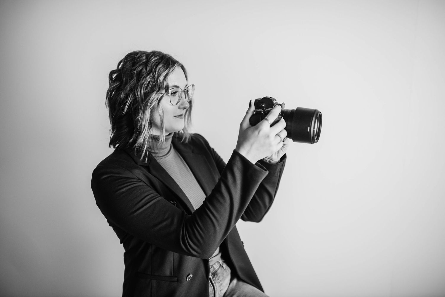 Black and white portrait of photographer with camera against minimalist background.