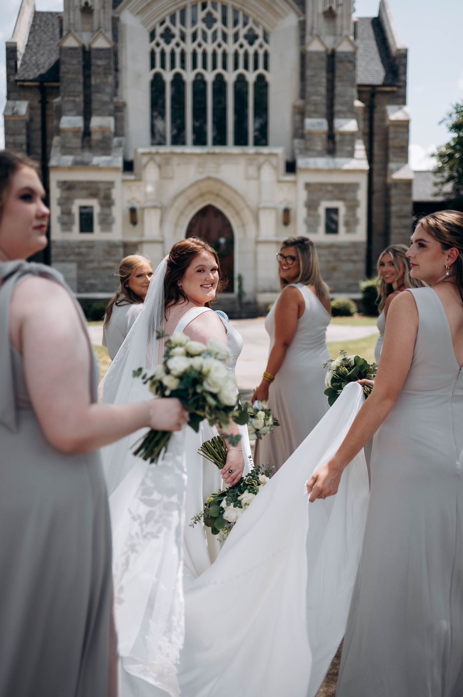 Wedding party poses in front of gothic church architecture holding white floral bouquets.