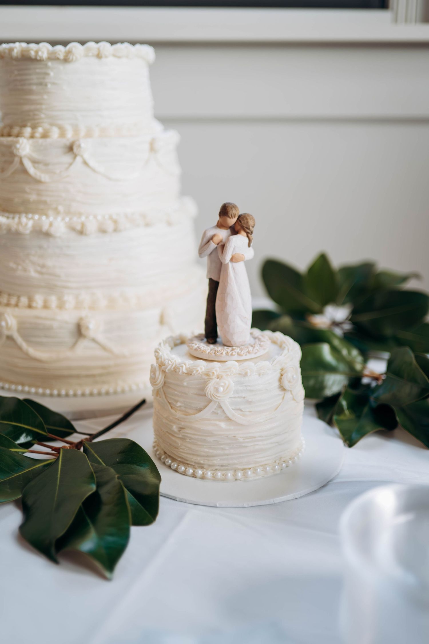 Elegant white wedding cake with delicate piping and a miniature bride and groom topper.