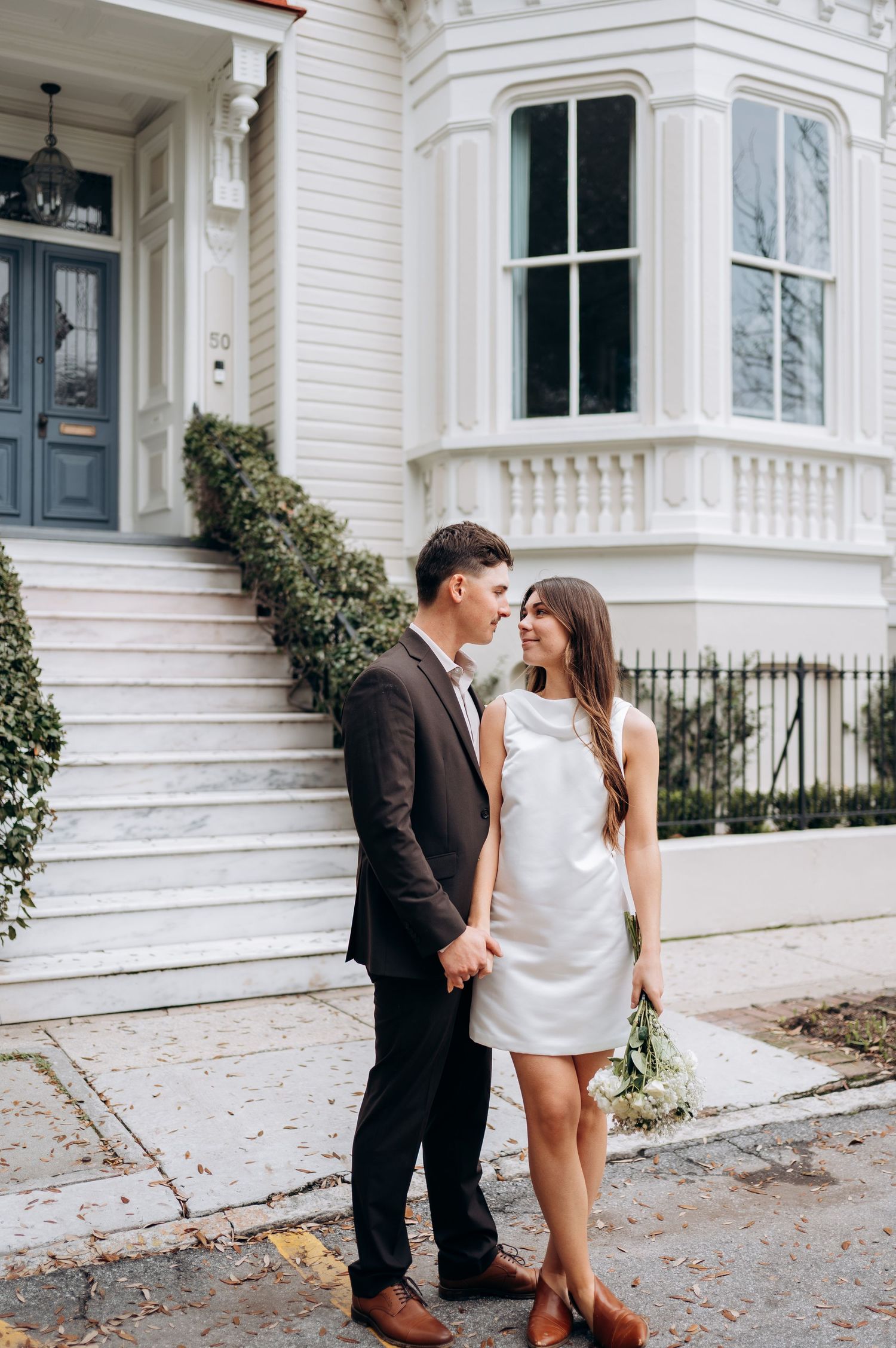 Couple sharing tender moments outside a classic white Victorian house.