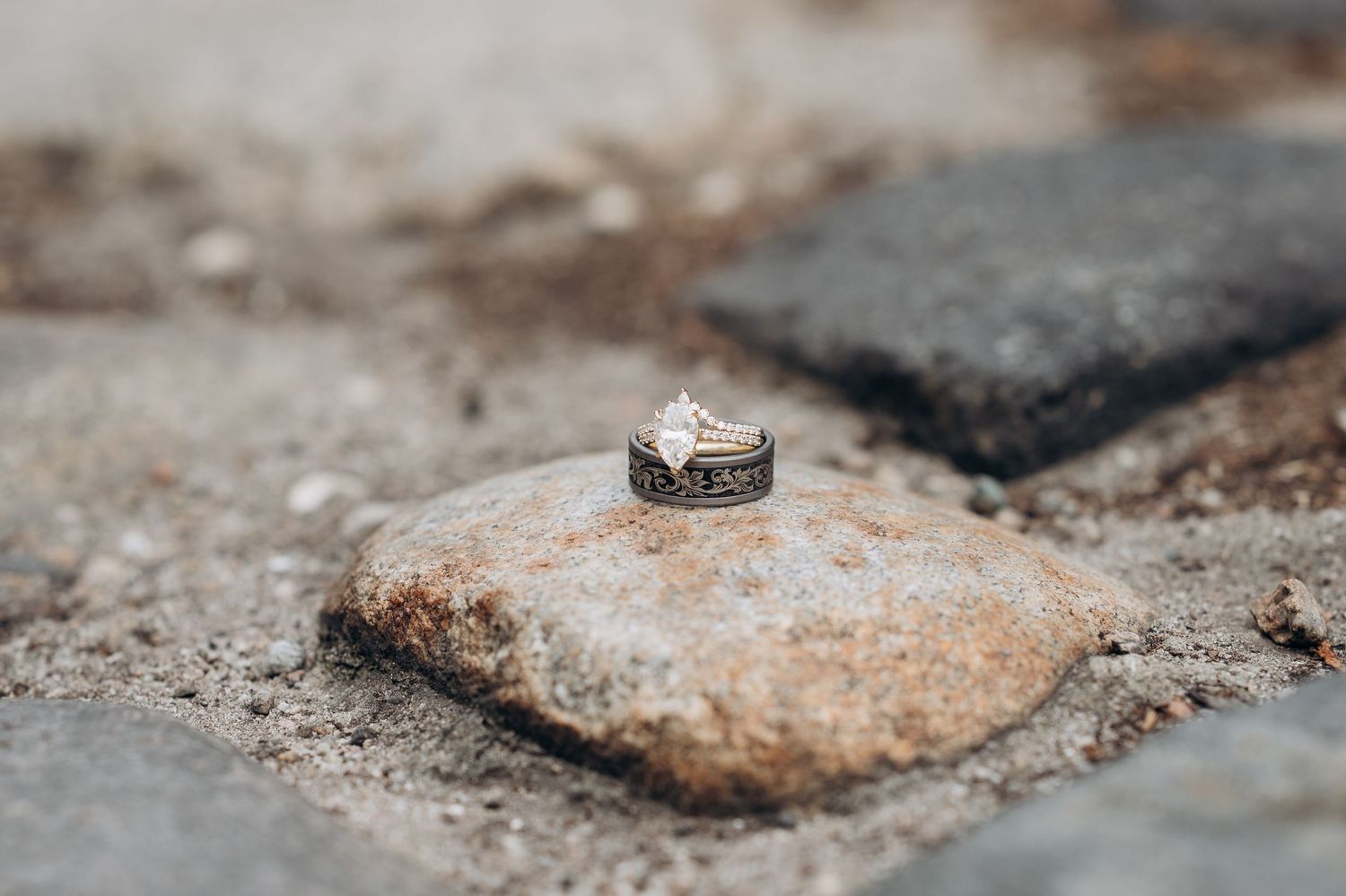 Close-up of a diamond engagement ring resting on a rustic stone outdoors.