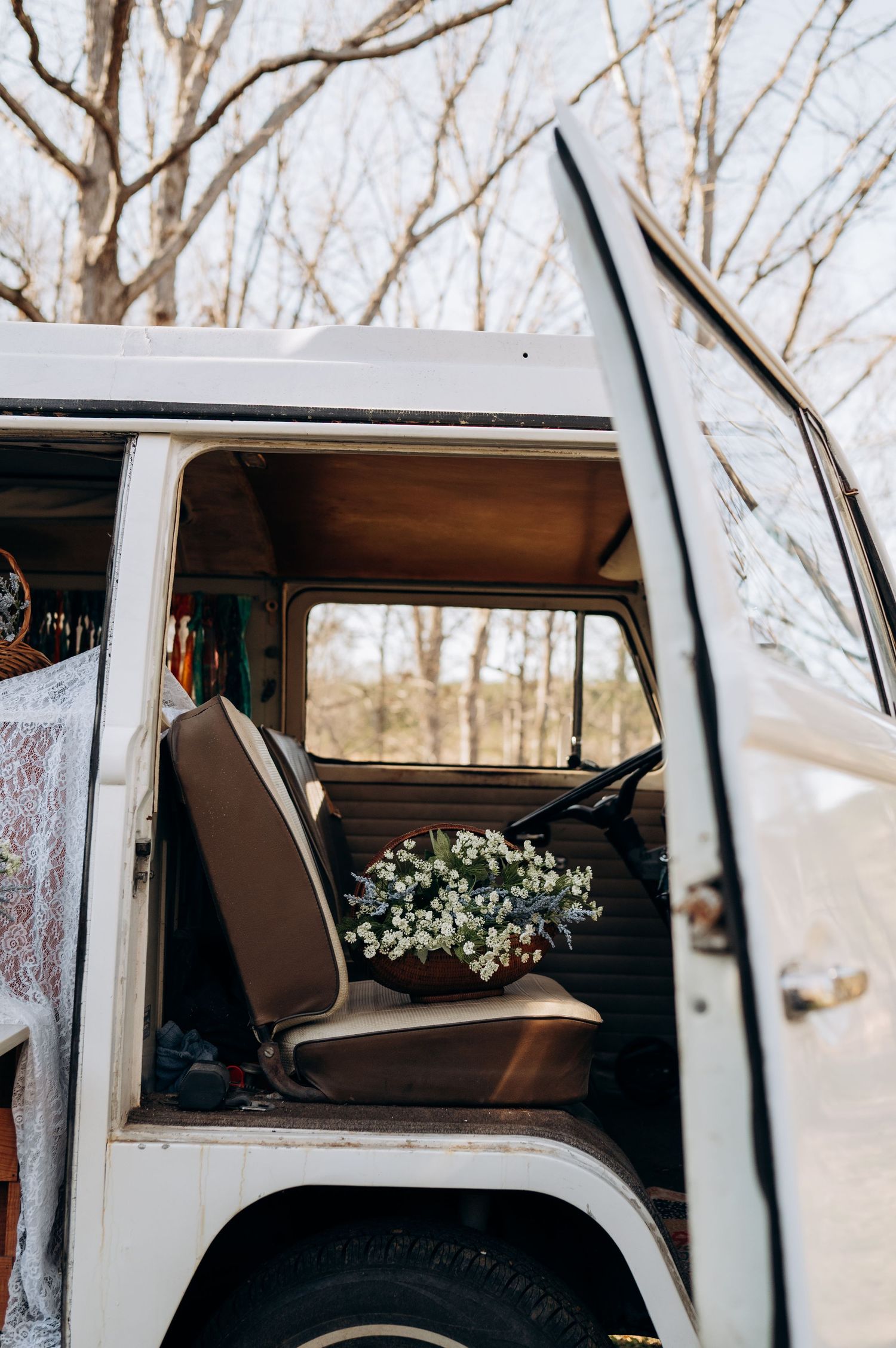 White flowers decorate the interior of a vintage Volkswagen van with bare winter trees visible through the windows.