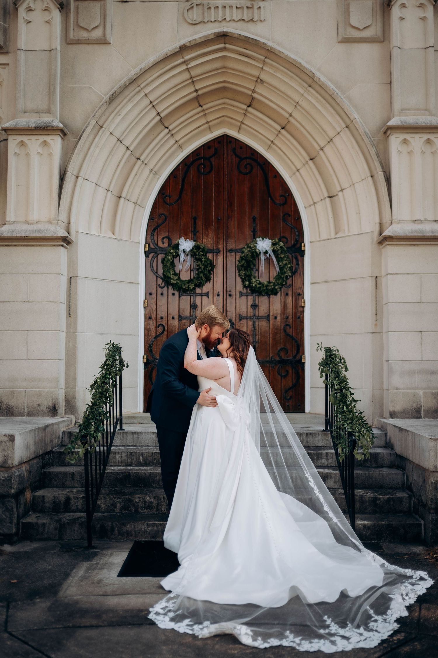 Wedding couple embracing in front of gothic church entrance with flowing white veil.