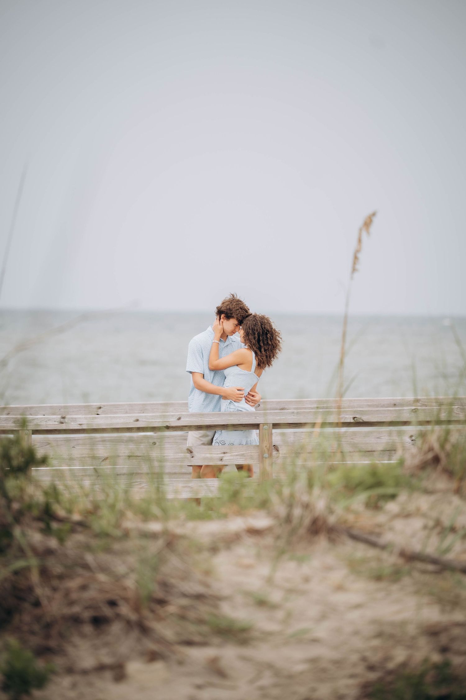Couple embraces on wooden boardwalk at misty beach.