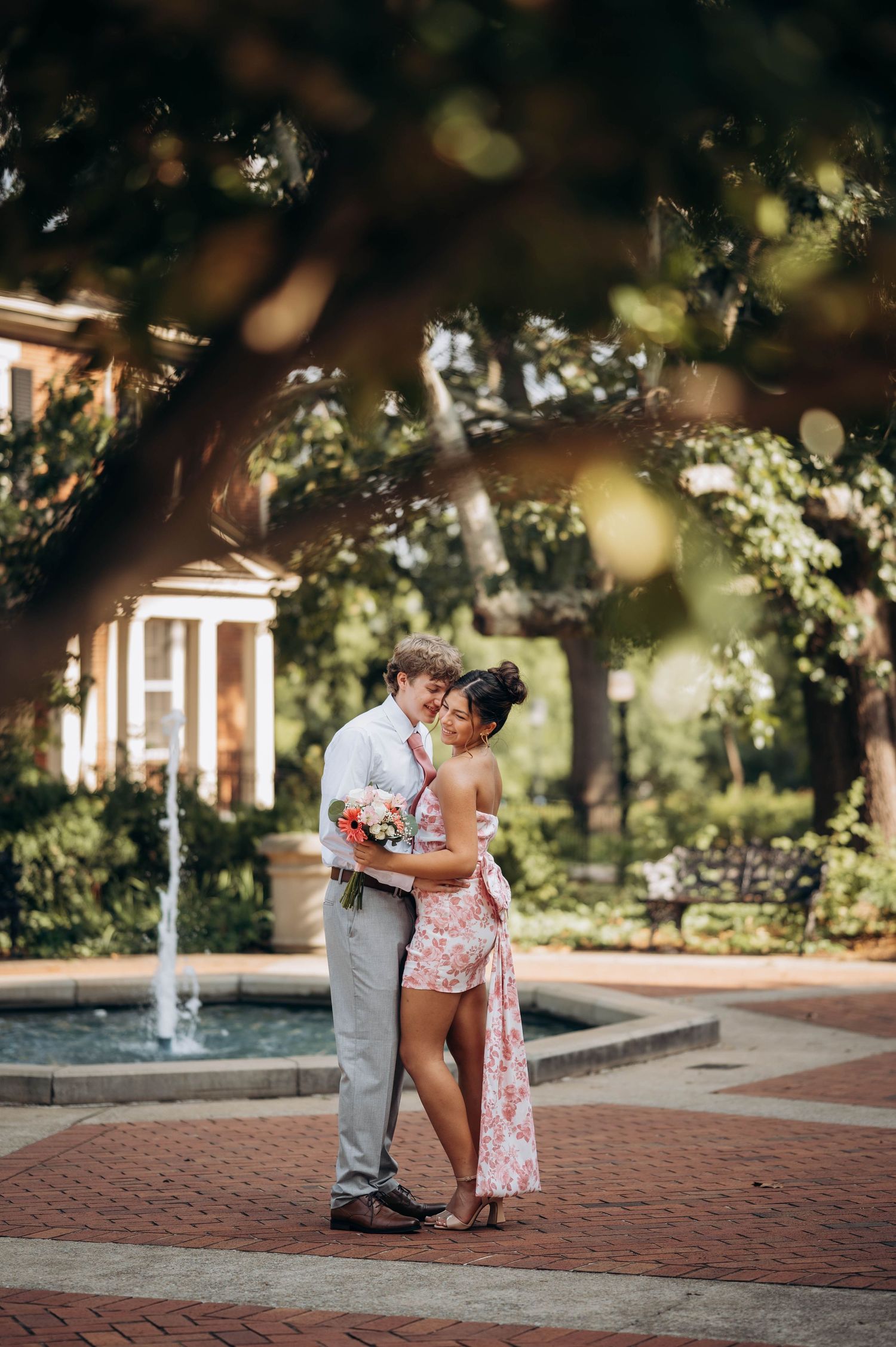 A couple shares an intimate moment by a fountain in a scenic garden setting.