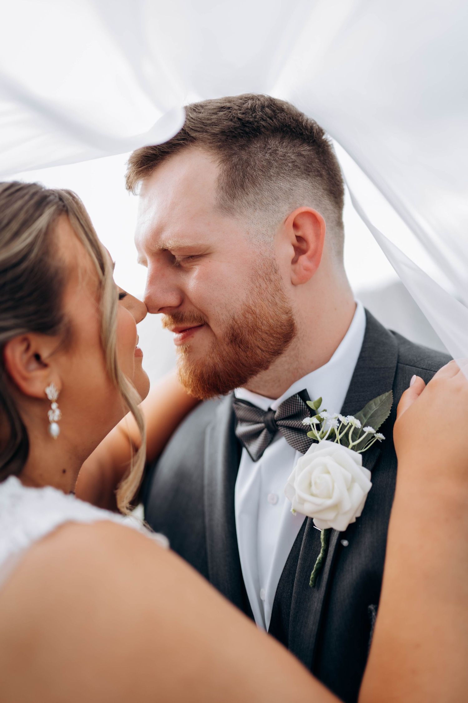 An intimate wedding moment captured under flowing white veil fabric.