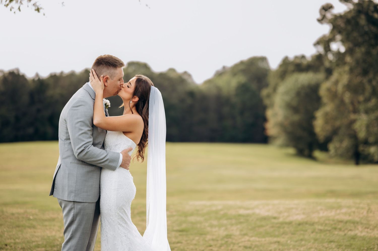 Bride and groom sharing a romantic kiss on a lush green lawn, bride wearing a white gown and veil.