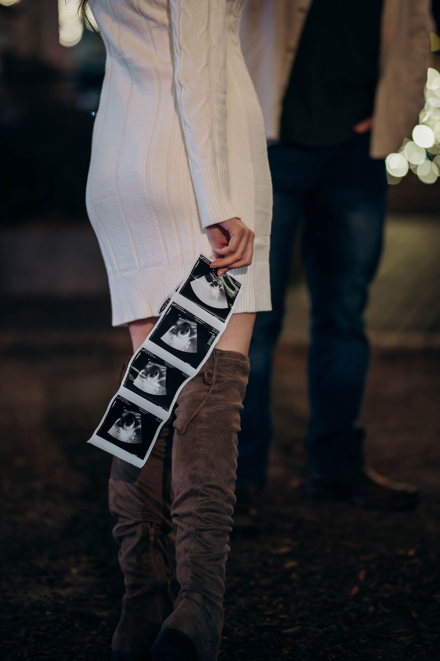 Woman holding ultrasound strip photos beside partner during holiday night pregnancy announcement.