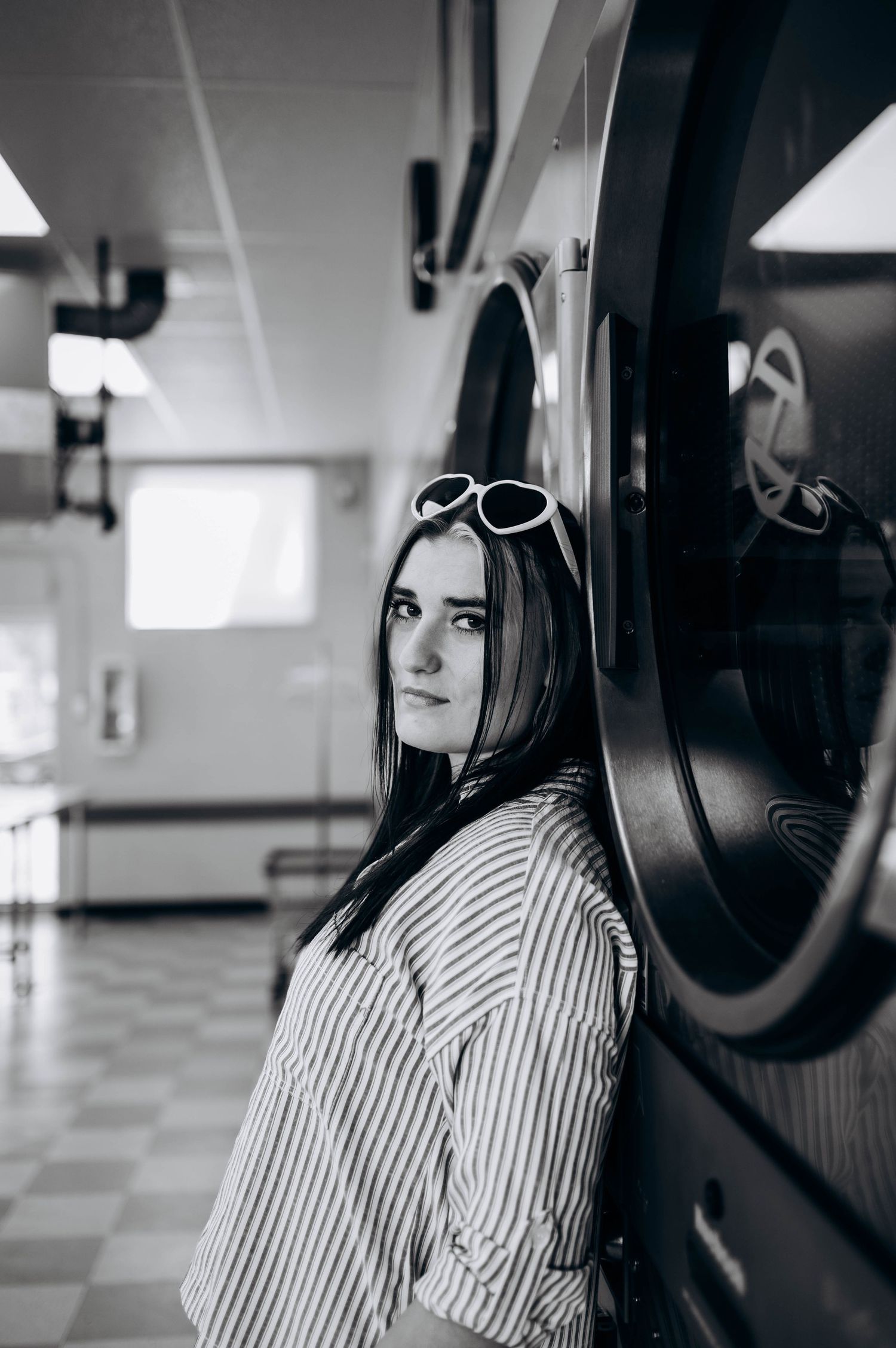 Moody black and white portraits of someone in striped clothing near laundry machines in an industrial space.