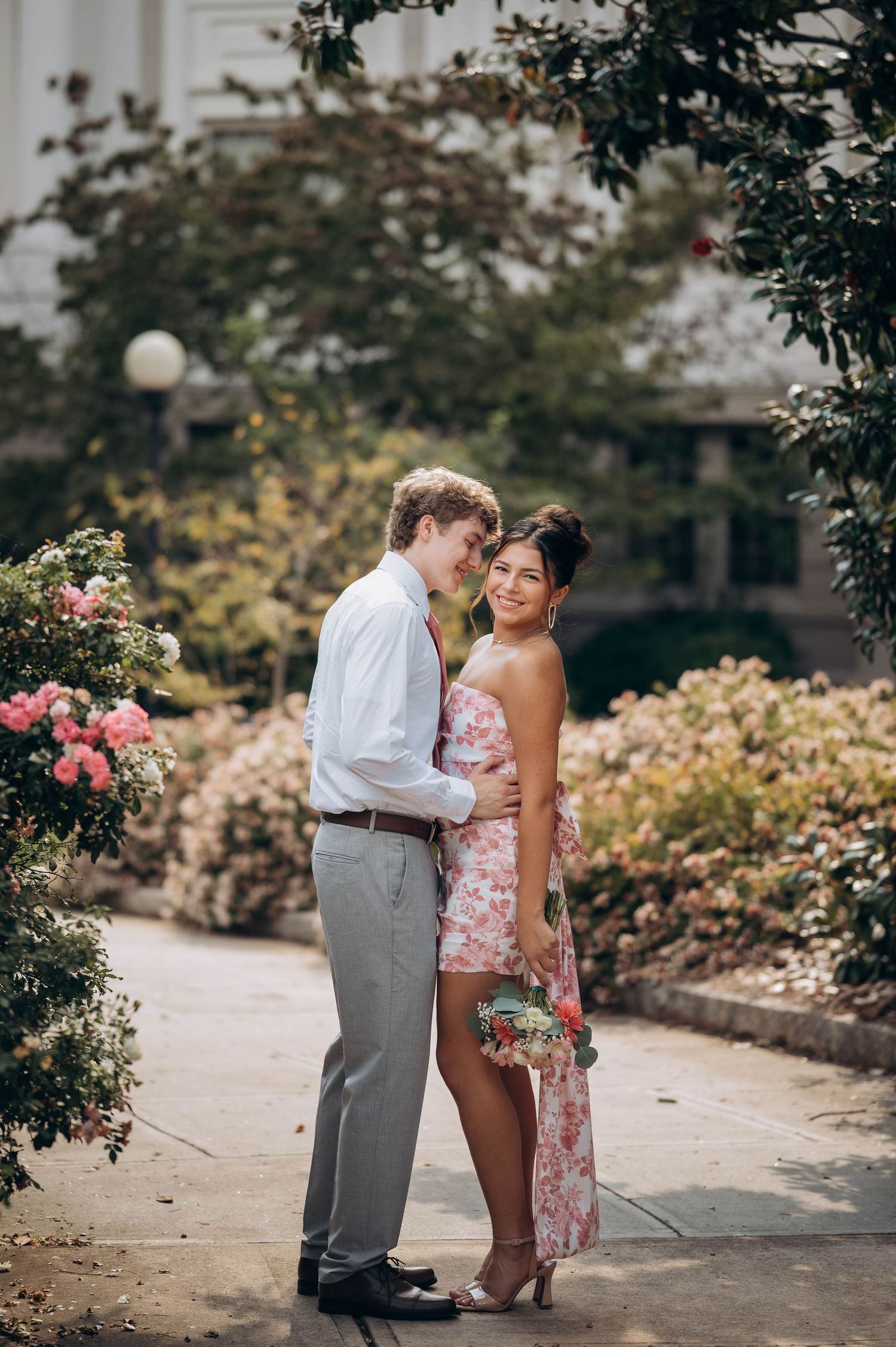 Couple posing together on a garden path with pink roses in bloom.