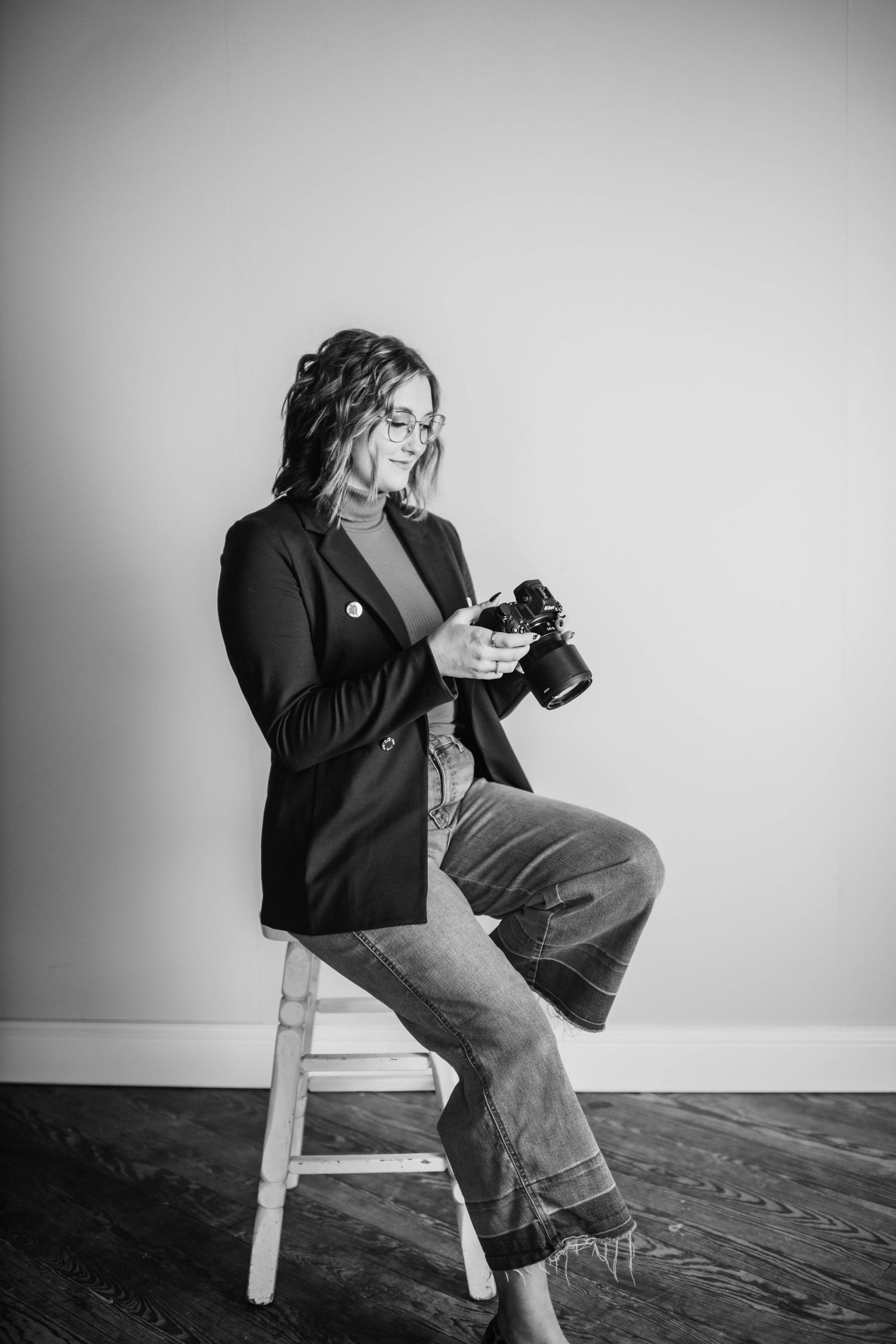 Black and white portrait of photographer sitting casually with camera in studio.