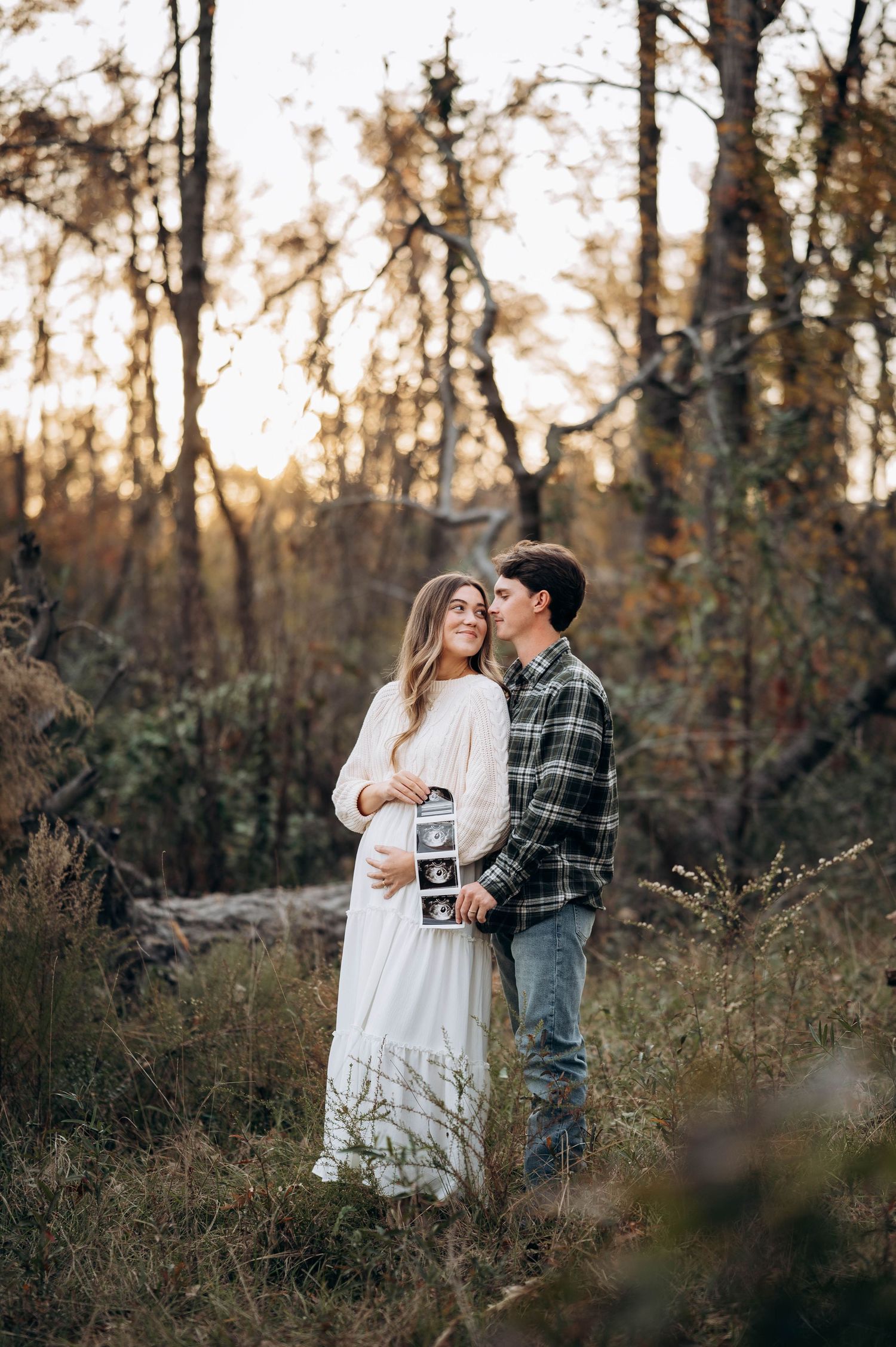 Couple holding ultrasound photos while sharing intimate moment in autumn forest.