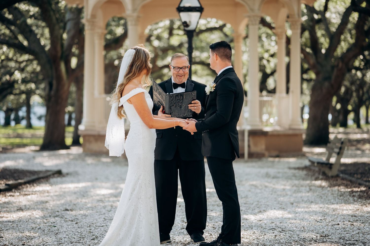 Bride and groom exchanging vows with officiant at outdoor gazebo wedding ceremony.