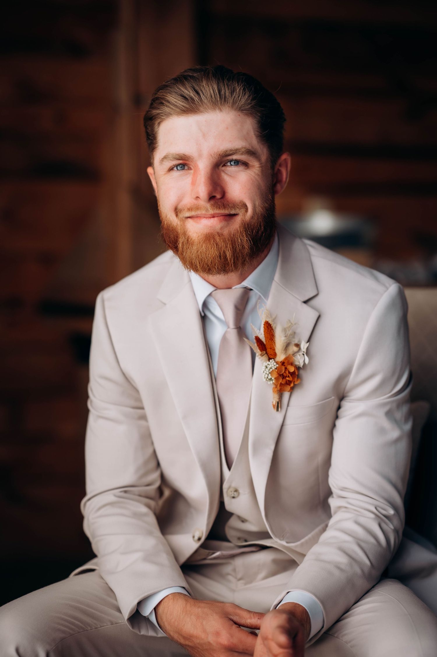 Groom in light gray suit with orange boutonniere smiles during wedding portraits.