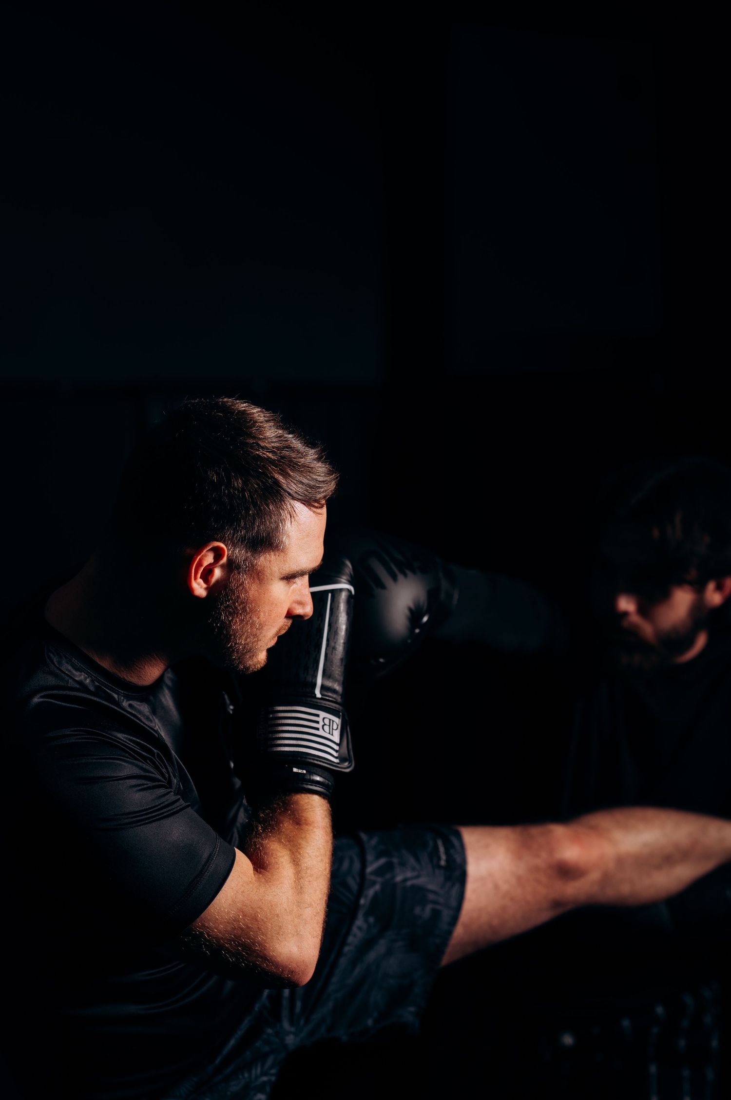 Athlete in dark clothing performs martial arts stance with focused intensity in dramatic lighting.
