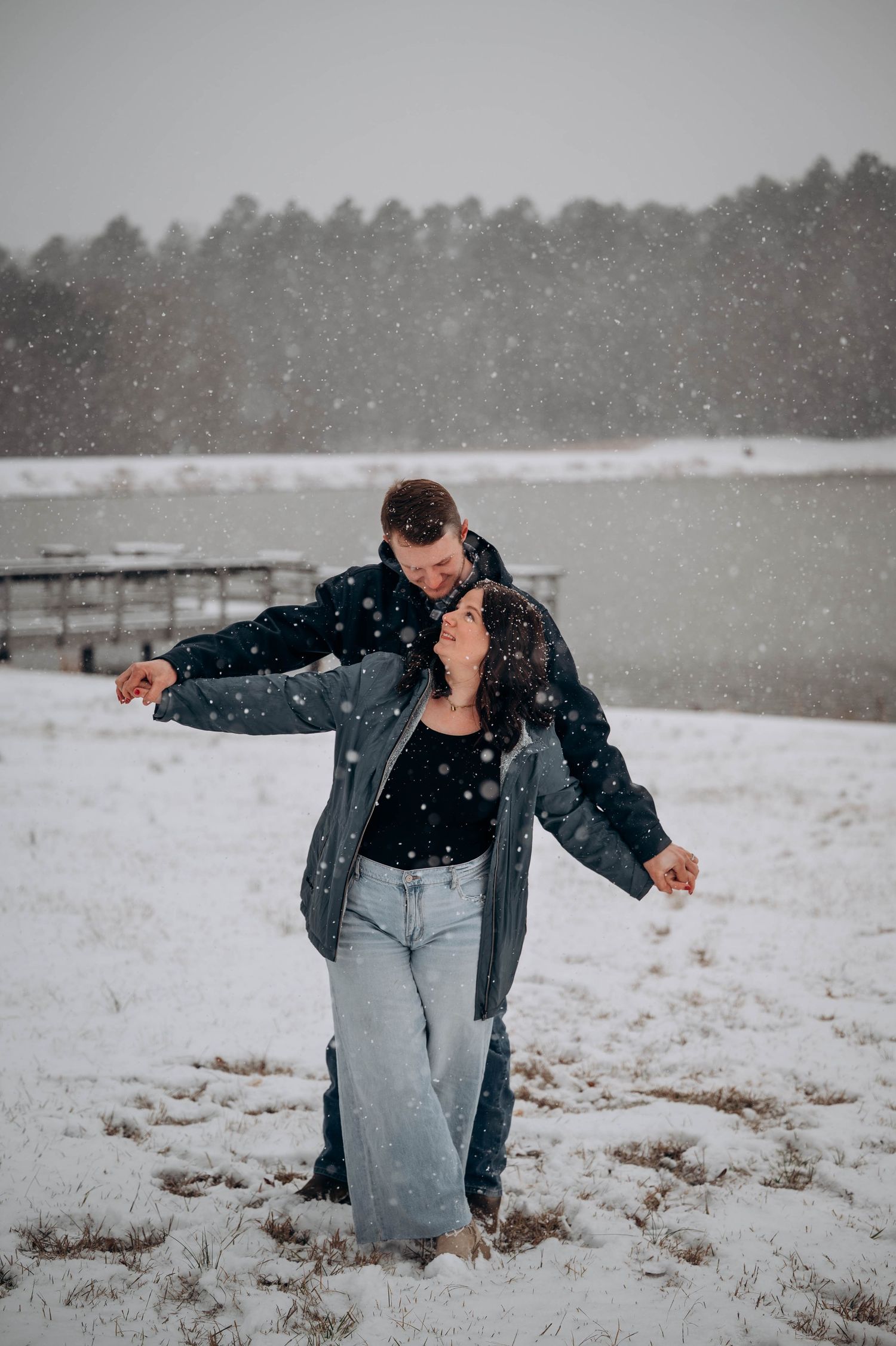 A person in a leather jacket and jeans dances playfully in a snowy field during winter weather.