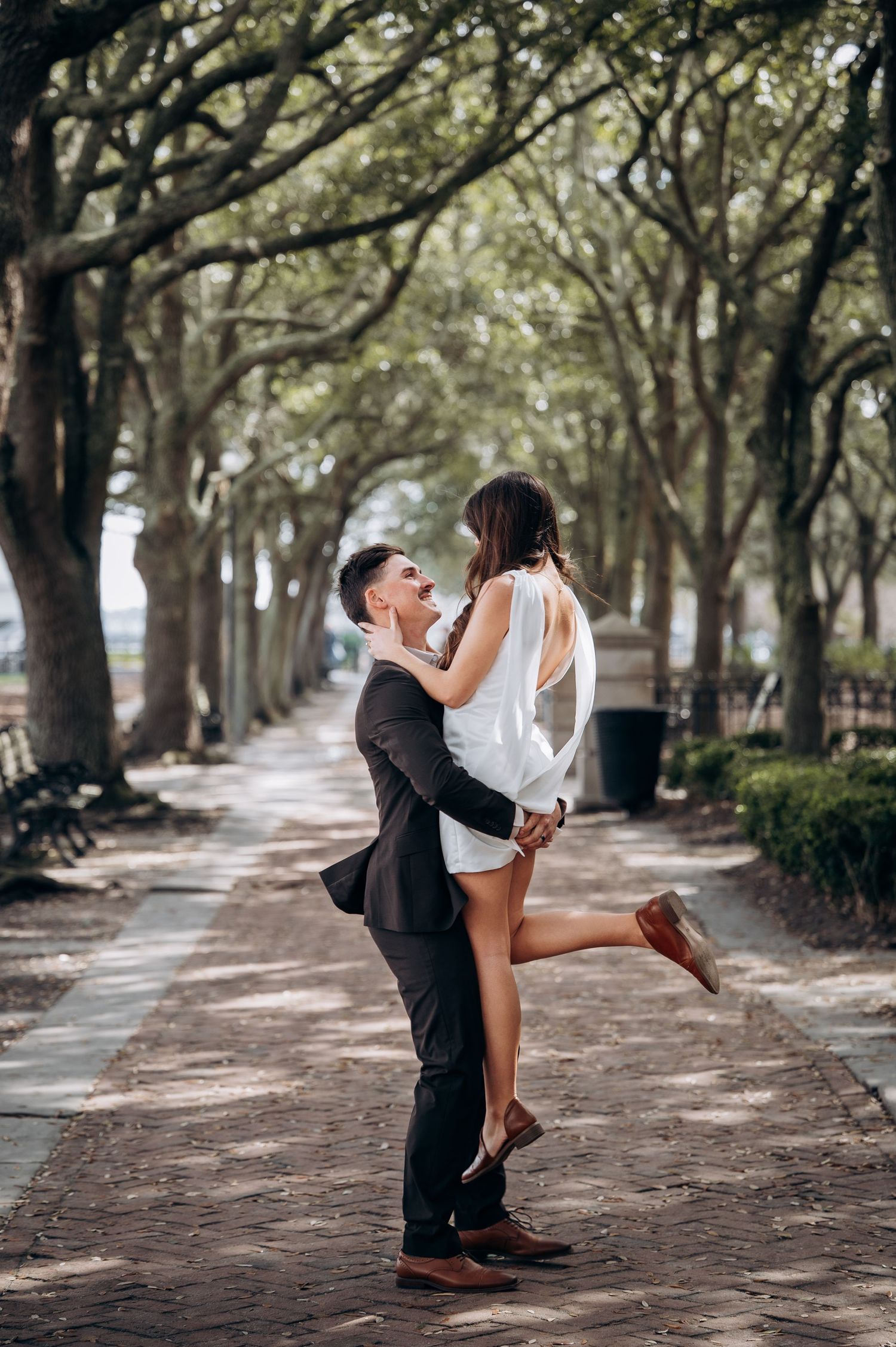 A couple in wedding attire sharing an intimate moment under a canopy of oak trees.