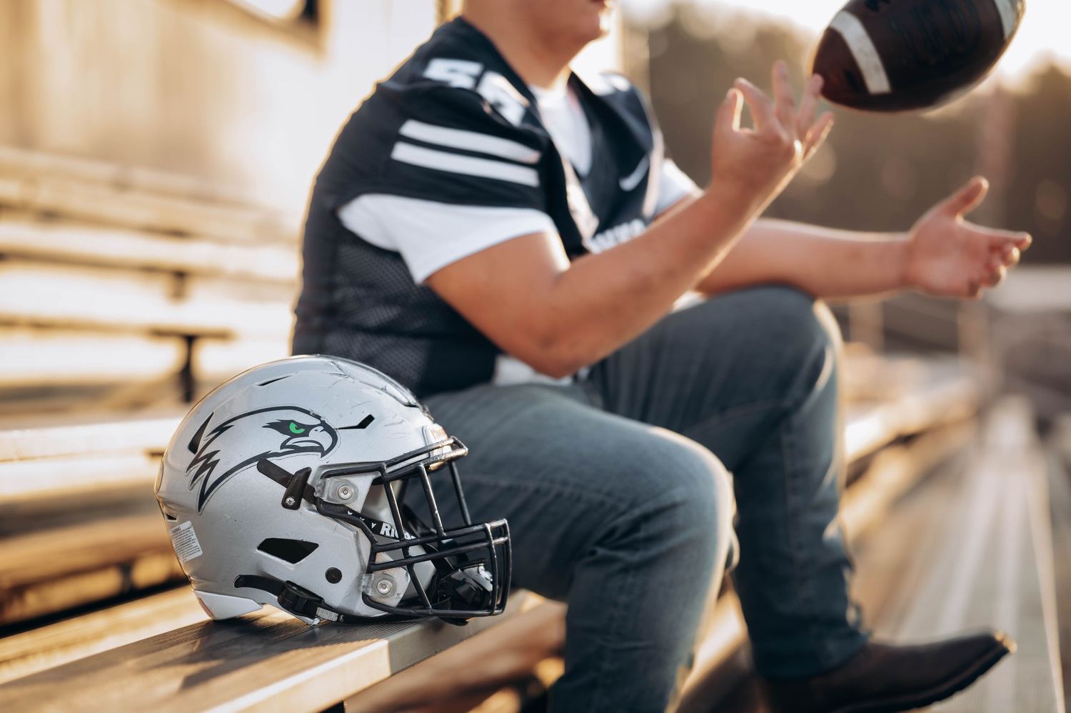Student athlete posing with football gear on metal bleachers during golden hour.