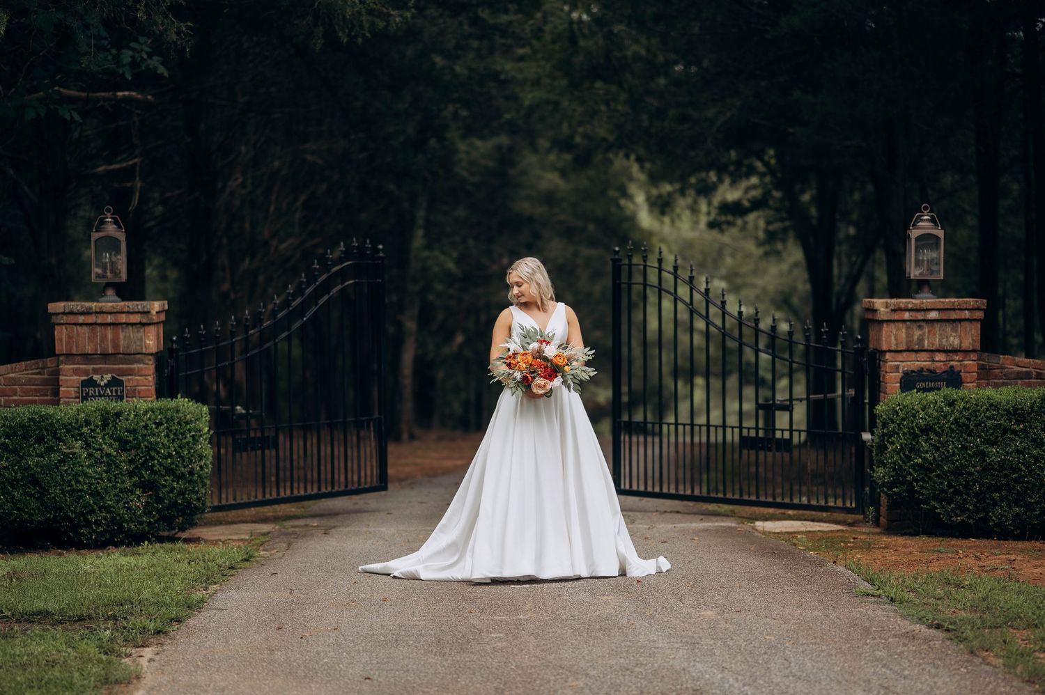 Bride in white ballgown poses on garden path with iron gates.