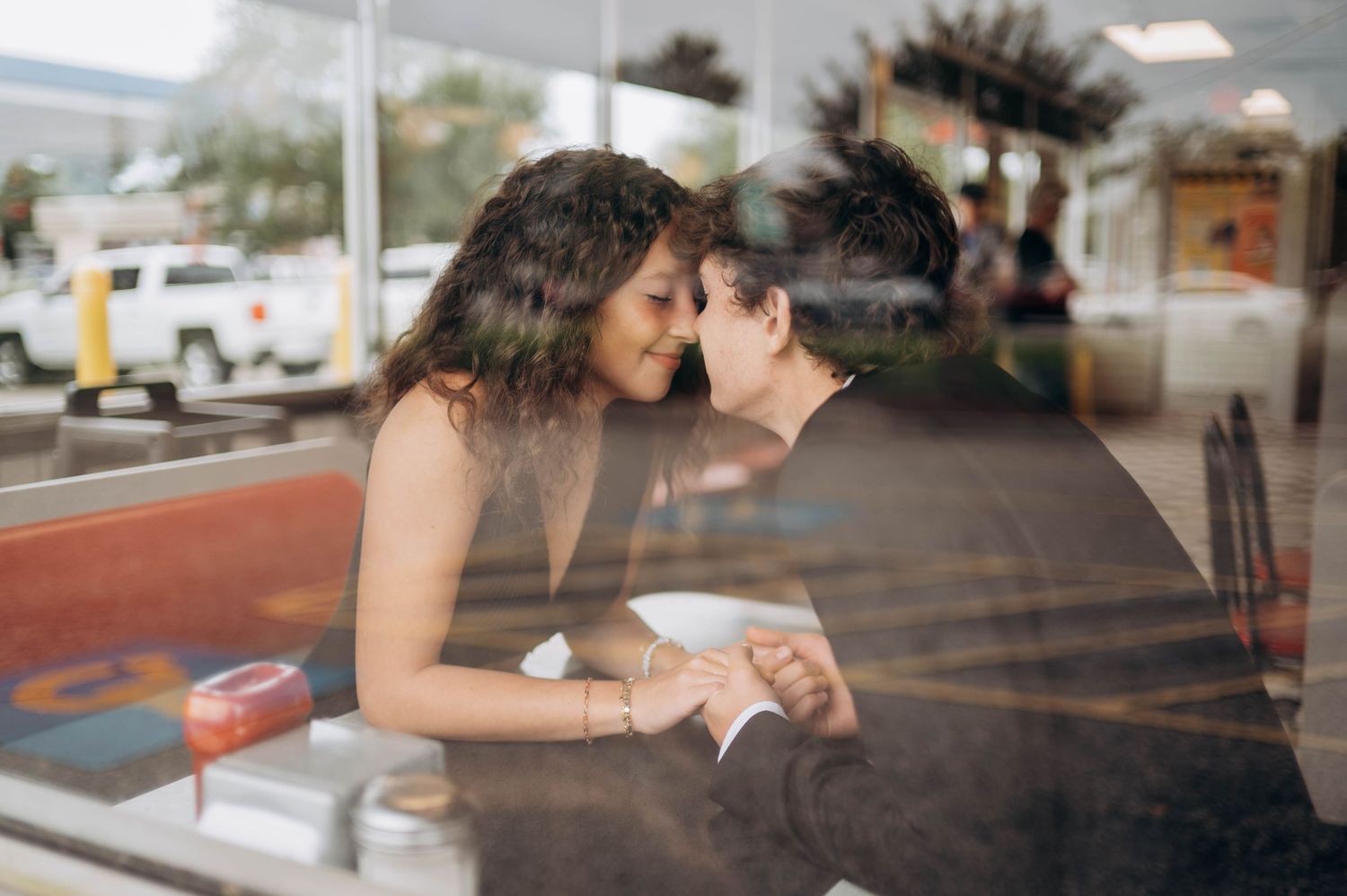 Couple sharing an intimate moment at a diner counter through window reflection.