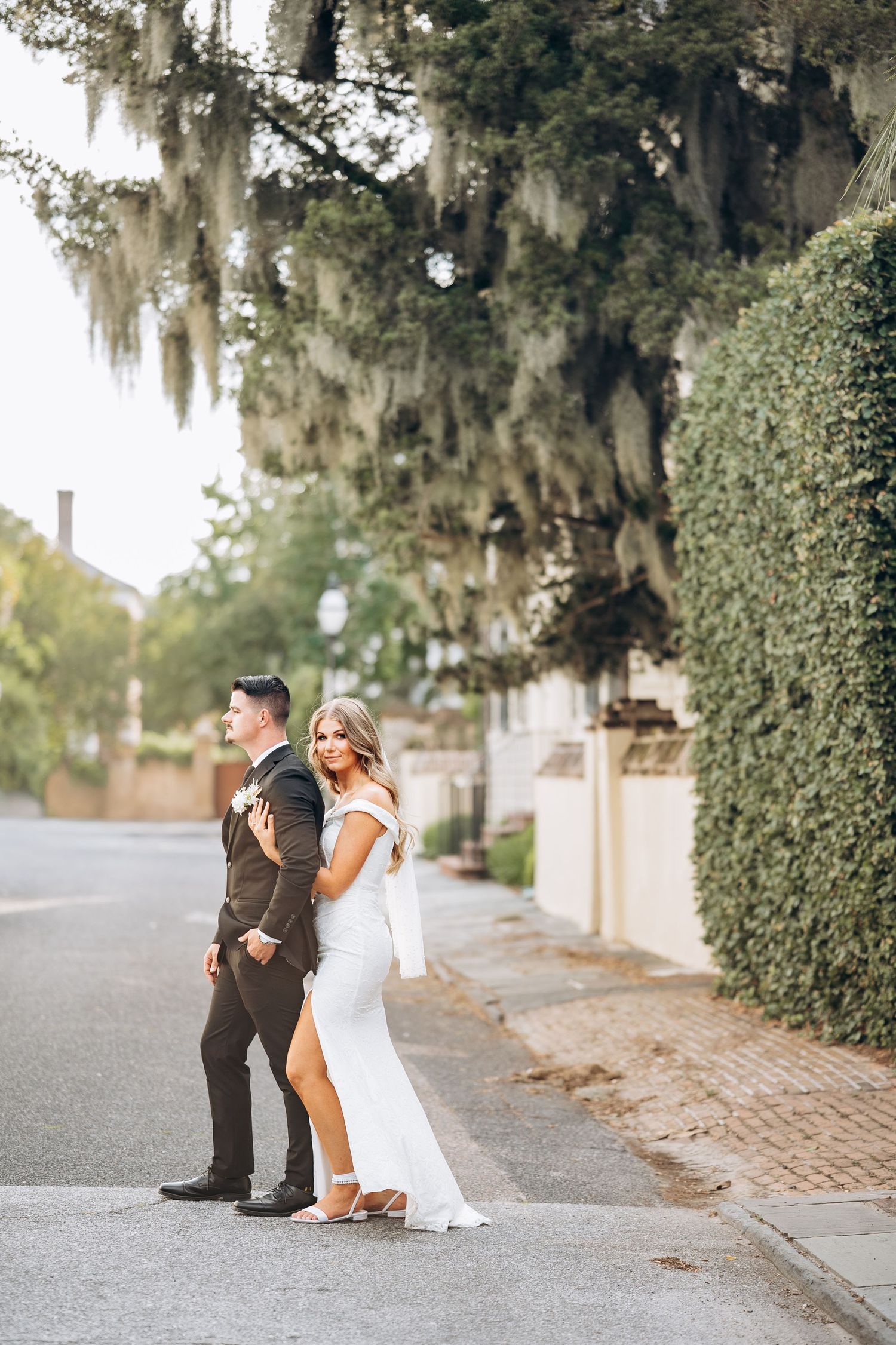 Bride and groom pose on tree-lined street draped with Spanish moss in Charleston, SC.