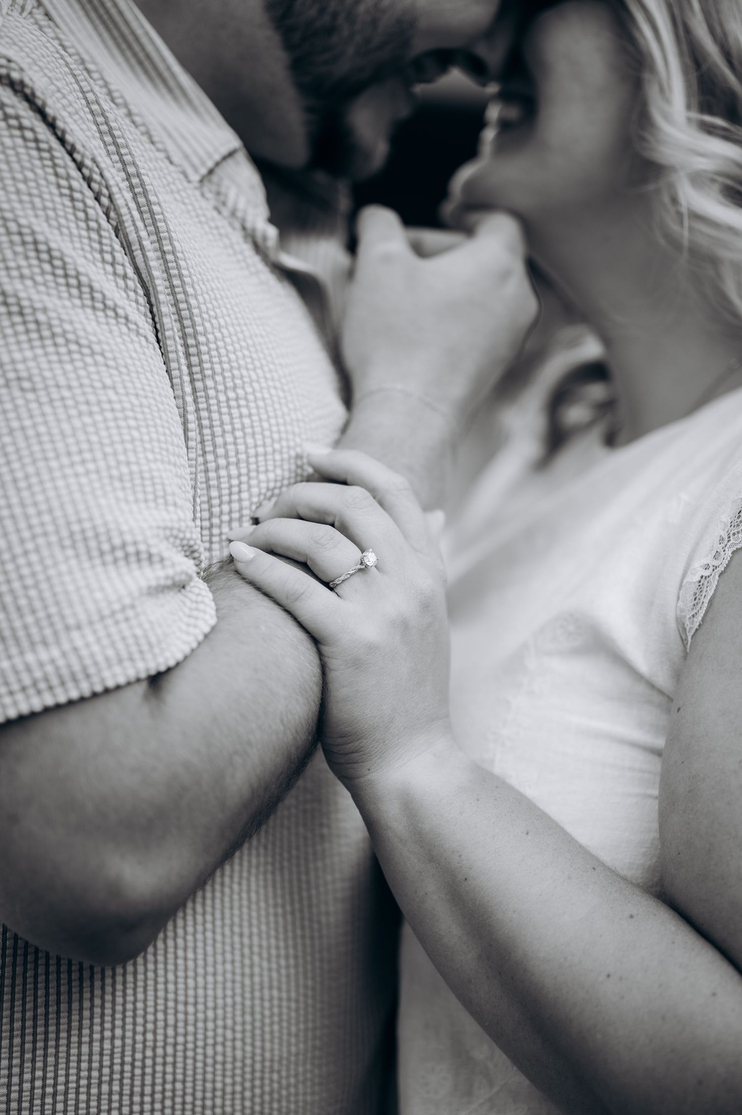 Black and white close-up of an engaged couple holding hands, showcasing a diamond engagement ring.