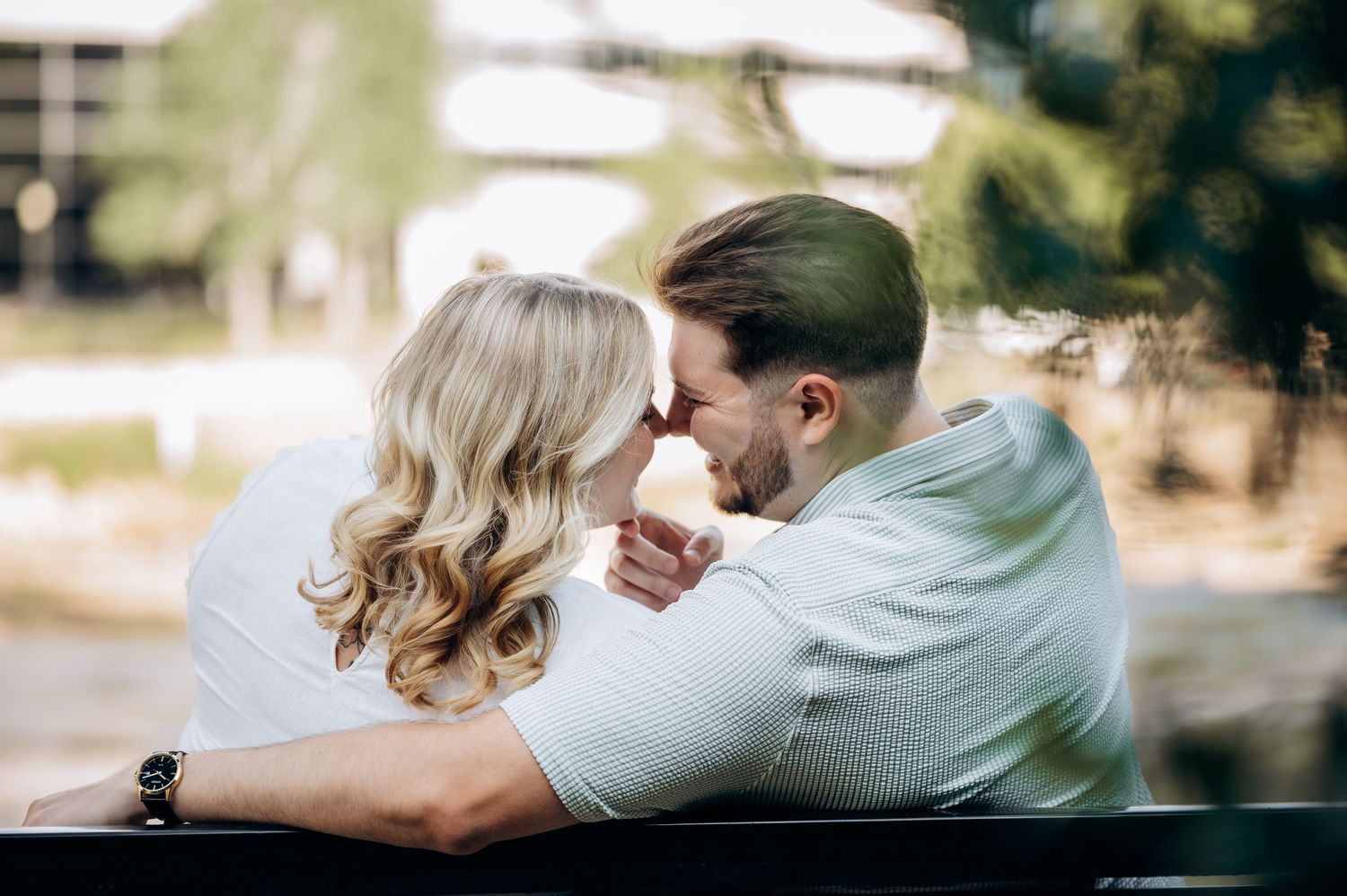 A romantic couple sharing an intimate moment, leaning close together outdoors with soft bokeh background.