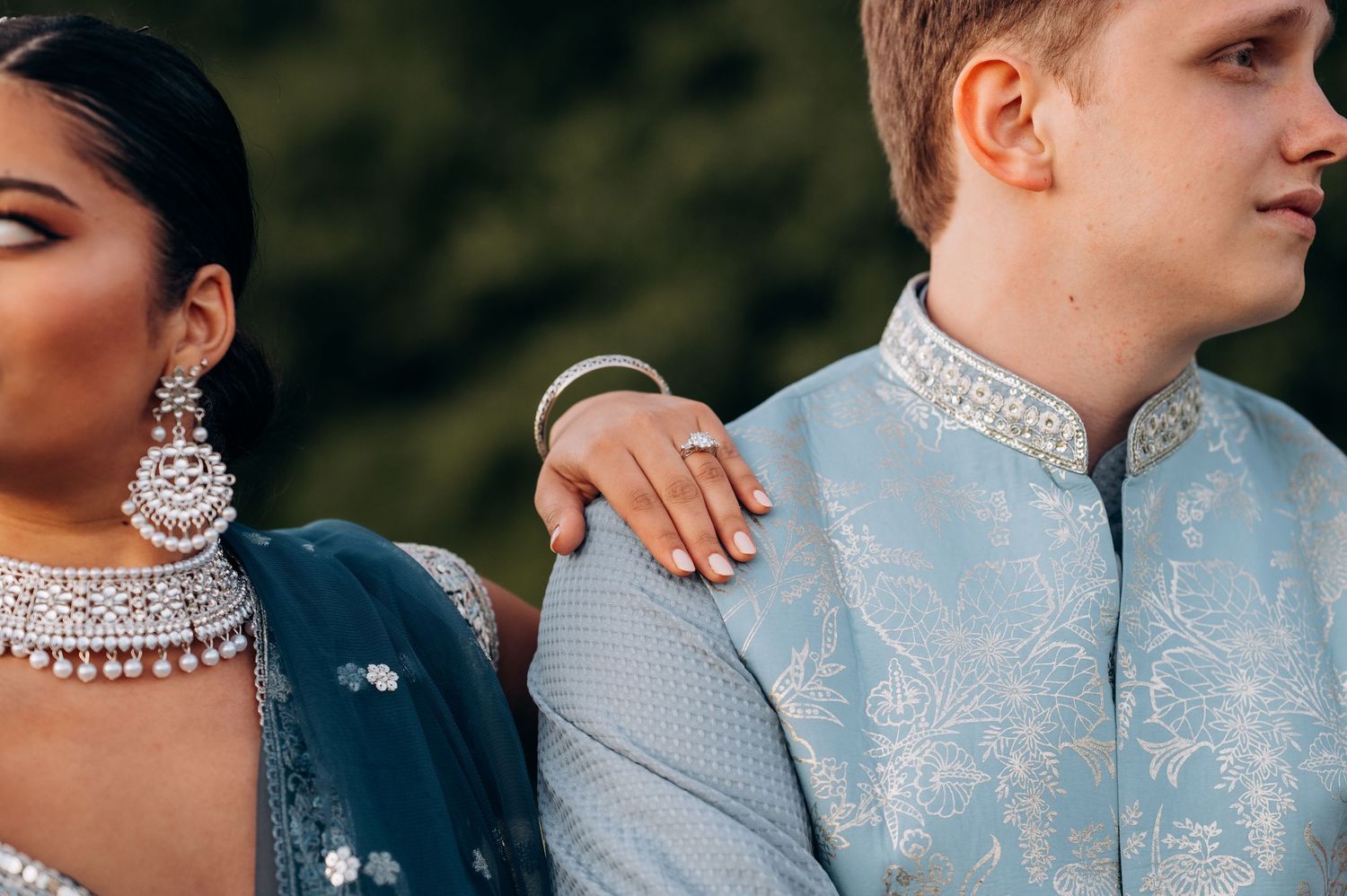 Couple in Indian wedding attire, woman in teal lehenga with diamond jewelry, man in light blue sherwani.