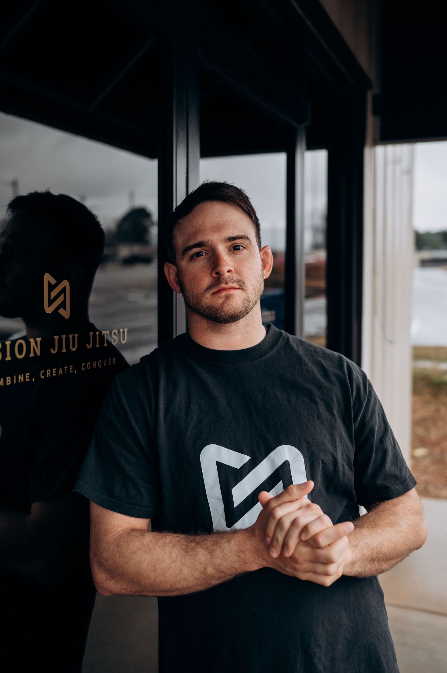 Person wearing black athletic apparel with white logo stands in front of jiu jitsu studio signage.