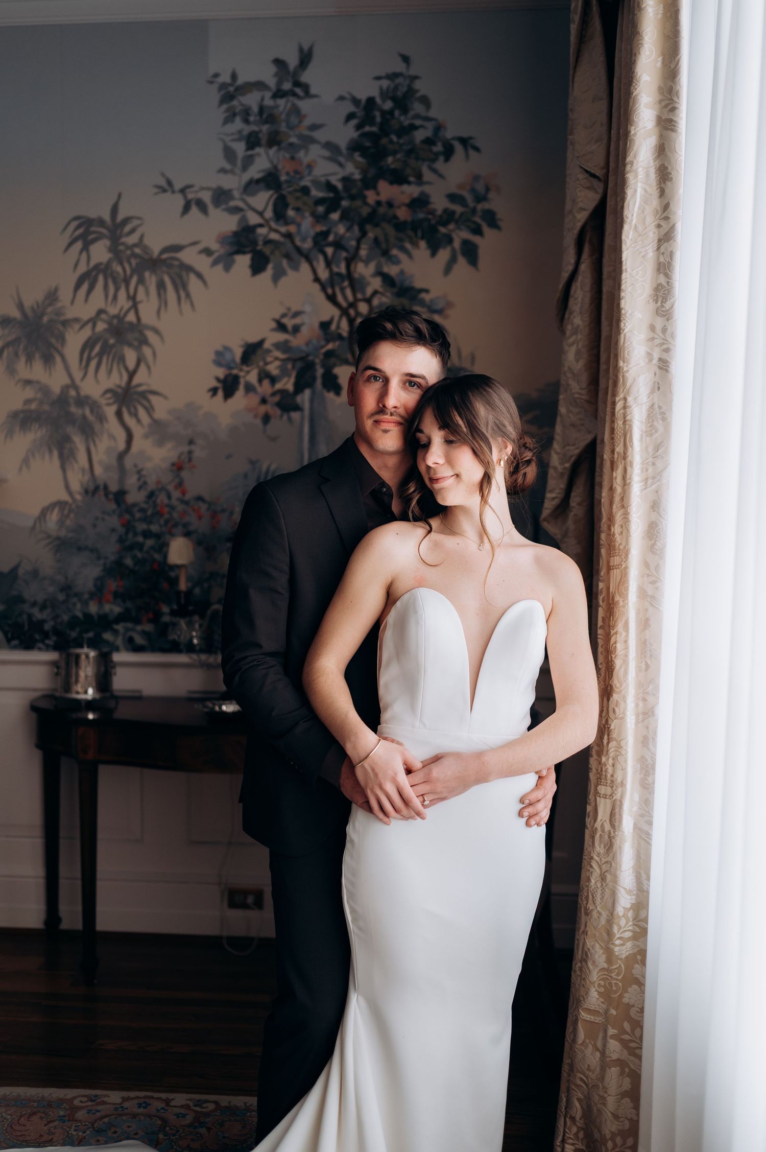 Elegant couple poses together in front of decorative wall mural featuring a romantic wedding photography moment.