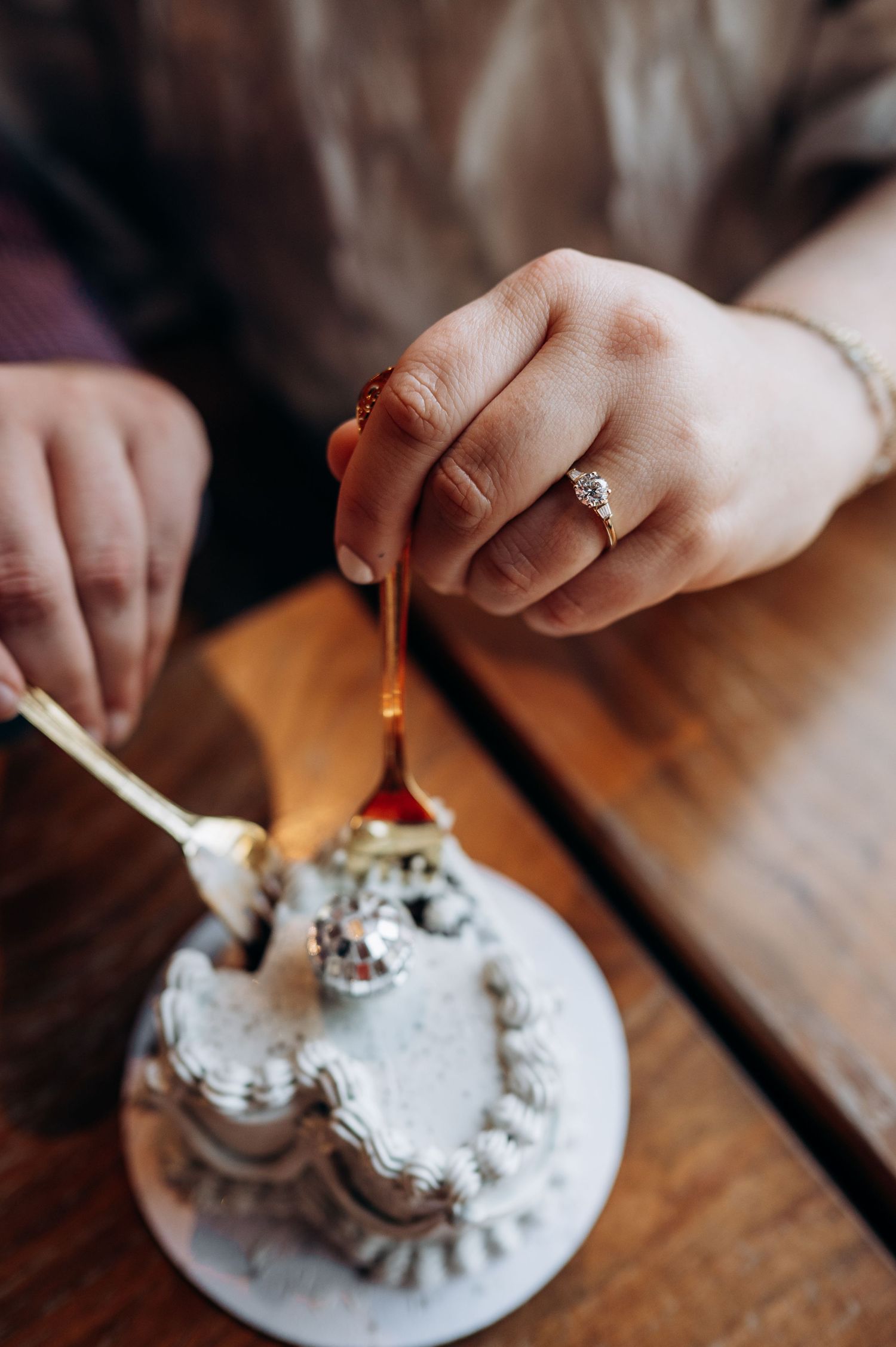Close-up of hands with engagement ring stirring a dessert topped with whipped cream on an ornate white plate.
