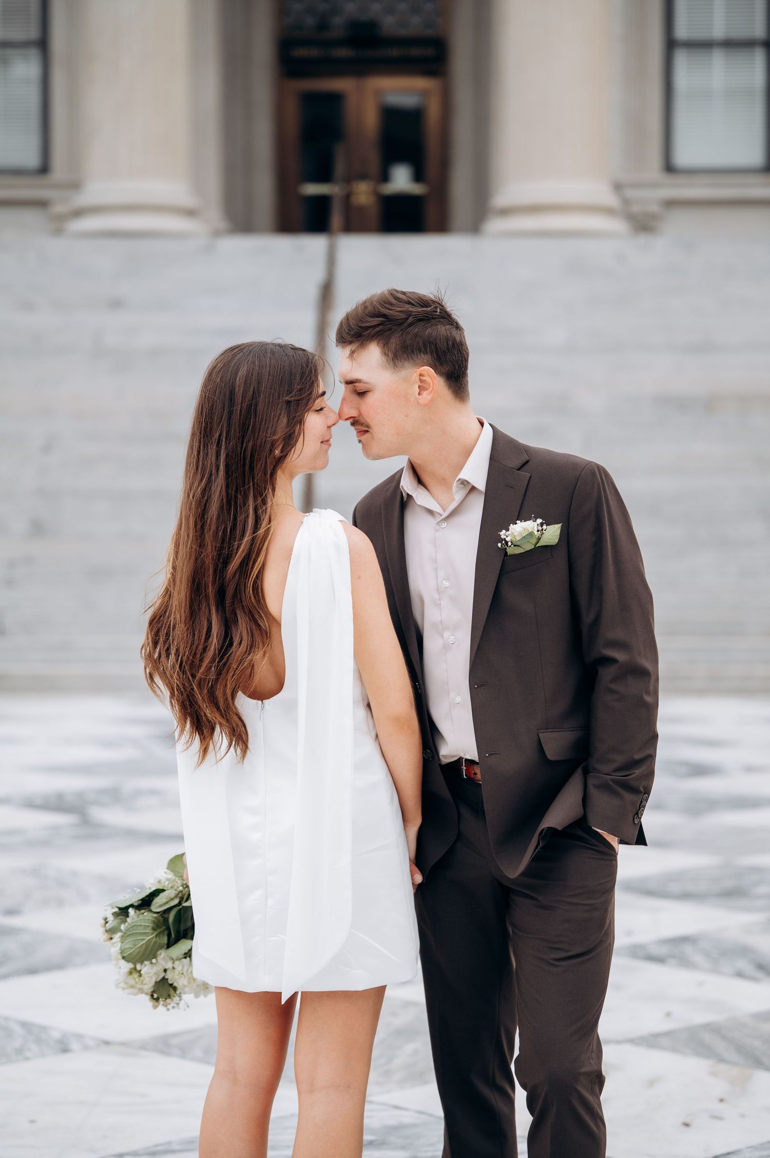 A romantic moment between newlyweds on marble steps with white columns in the background.