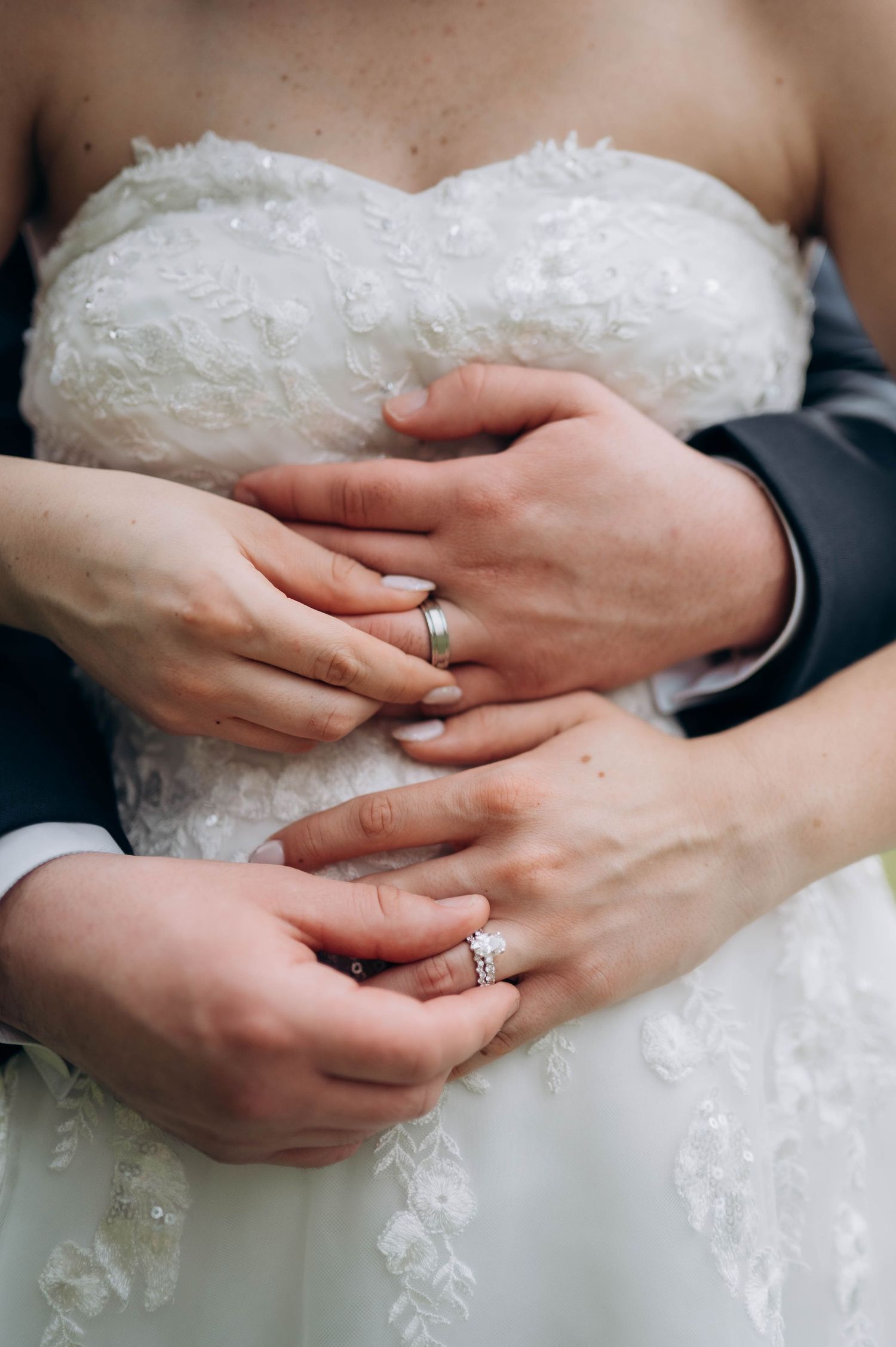 Close-up of newlywed couple's hands showing wedding rings against white lace dress.