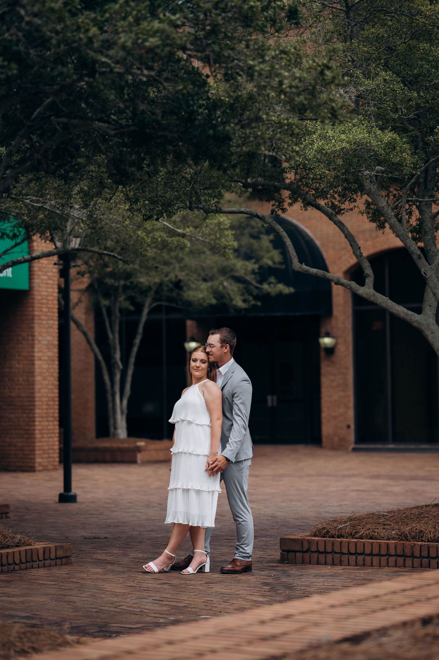 Romantic couple sharing intimate moments on brick paved courtyard surrounded by trees.
