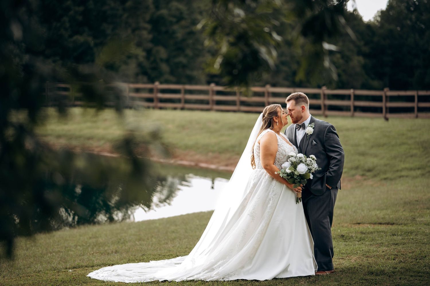 Wedding couple embraces during outdoor celebration with guests in background.