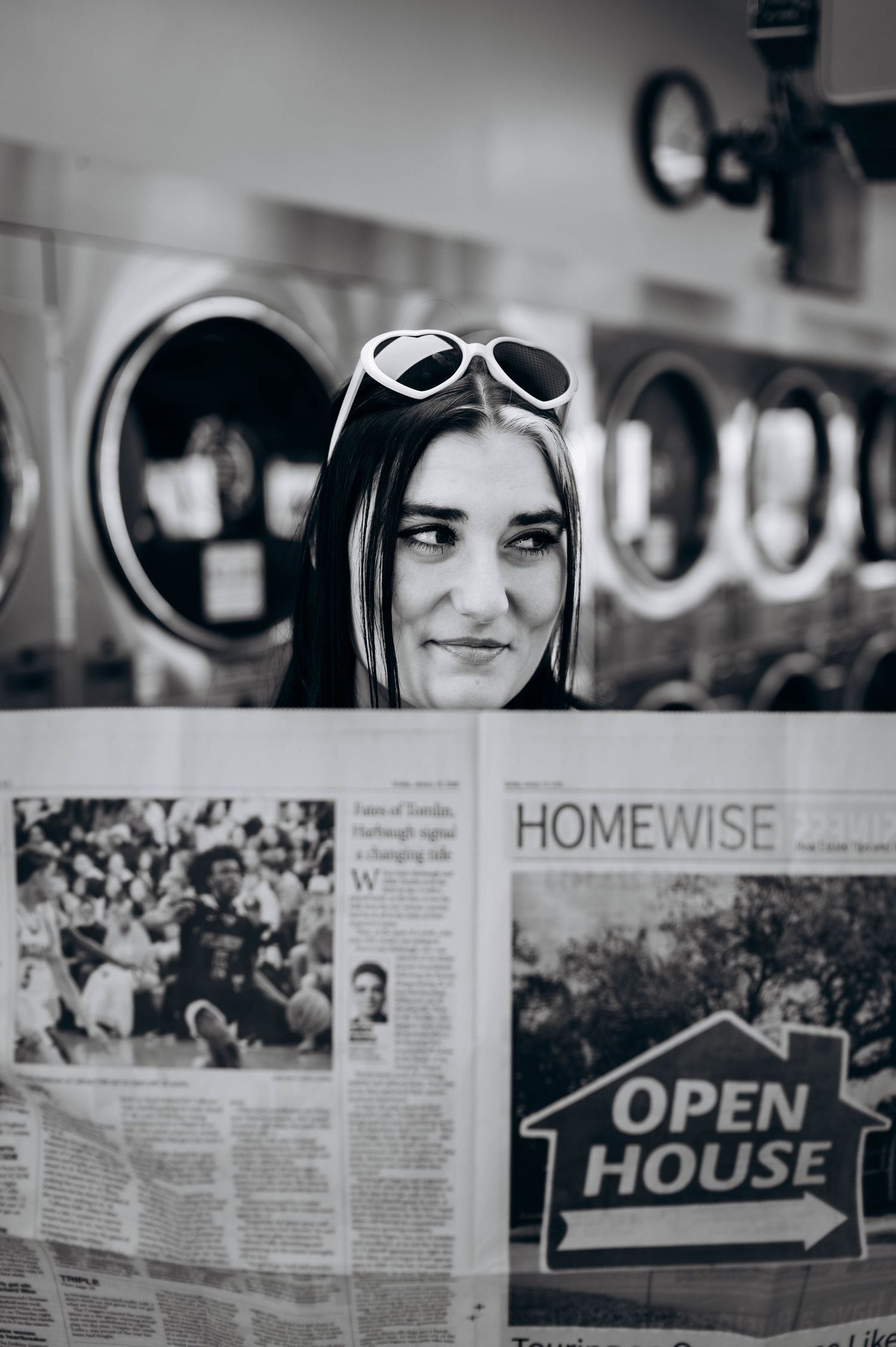 Person in sunglasses and striped shirt poses above newspaper headlines about home sales and open houses.