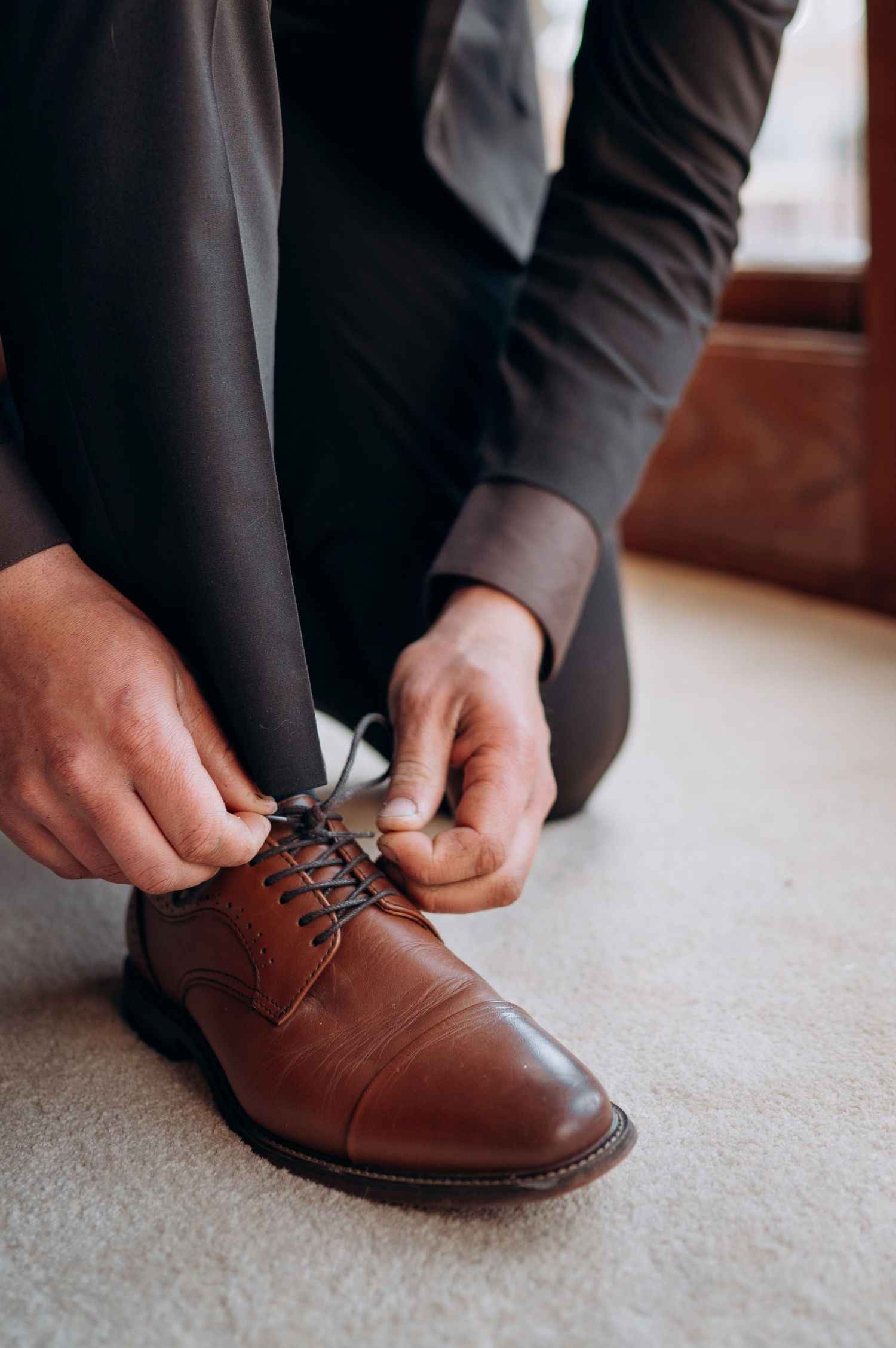 Close-up sequence of hands tying brown leather dress shoes on carpet.