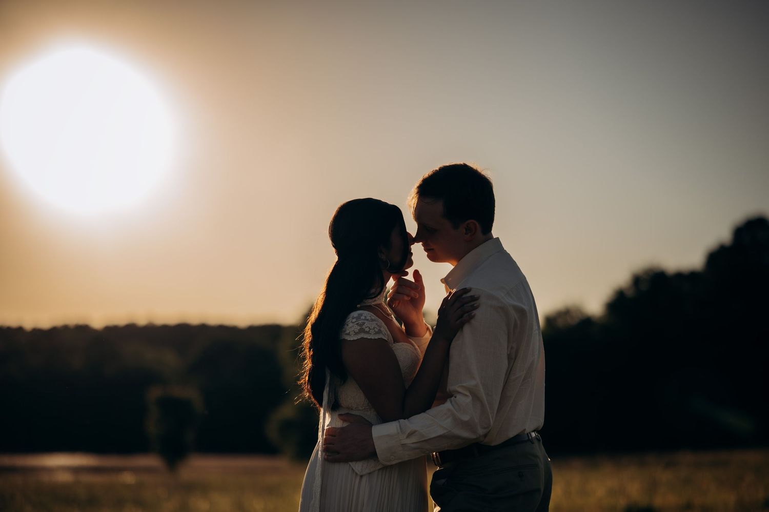 Couple sharing a romantic moment at golden hour sunset in an open field, silhouetted against warm glowing sun.