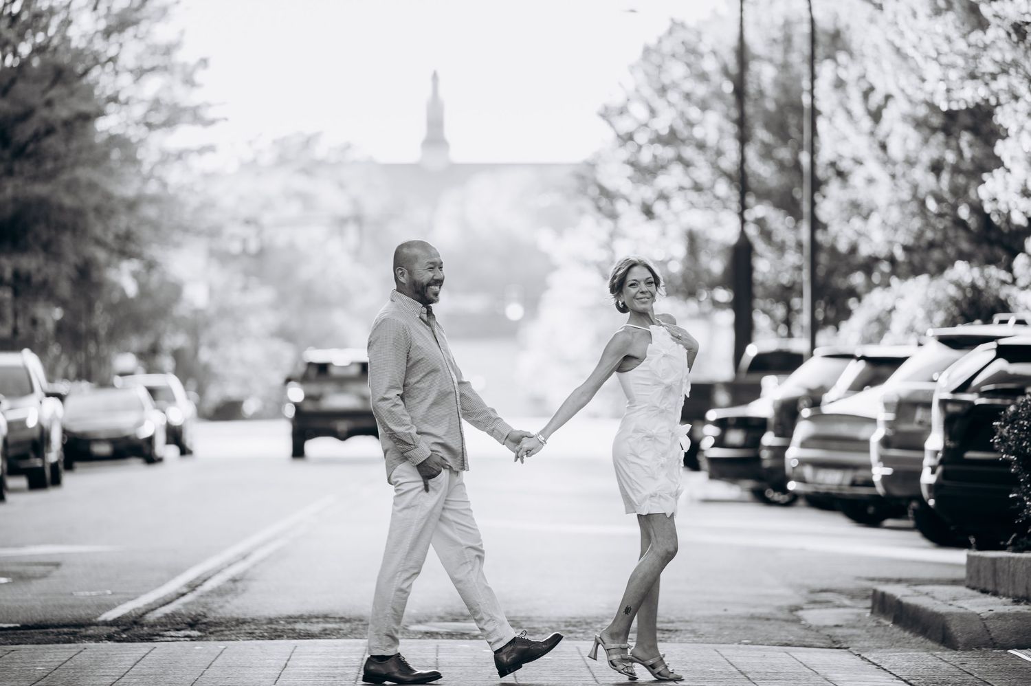 Black and white photo of a stylish couple holding hands while crossing a city street.