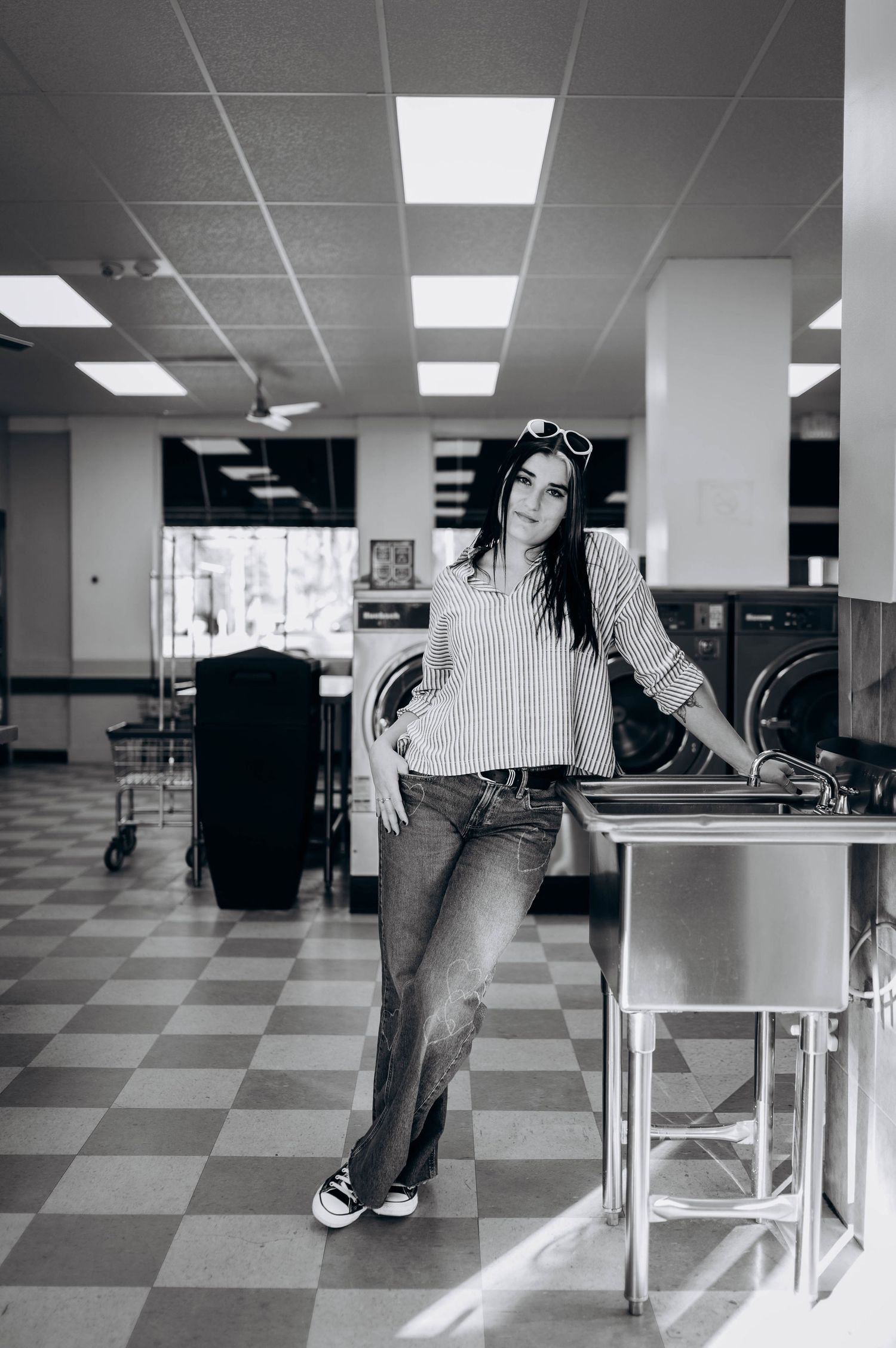 Black and white photo of a casual outfit at a laundromat with striped shirt, jeans and sneakers against checkered floor.