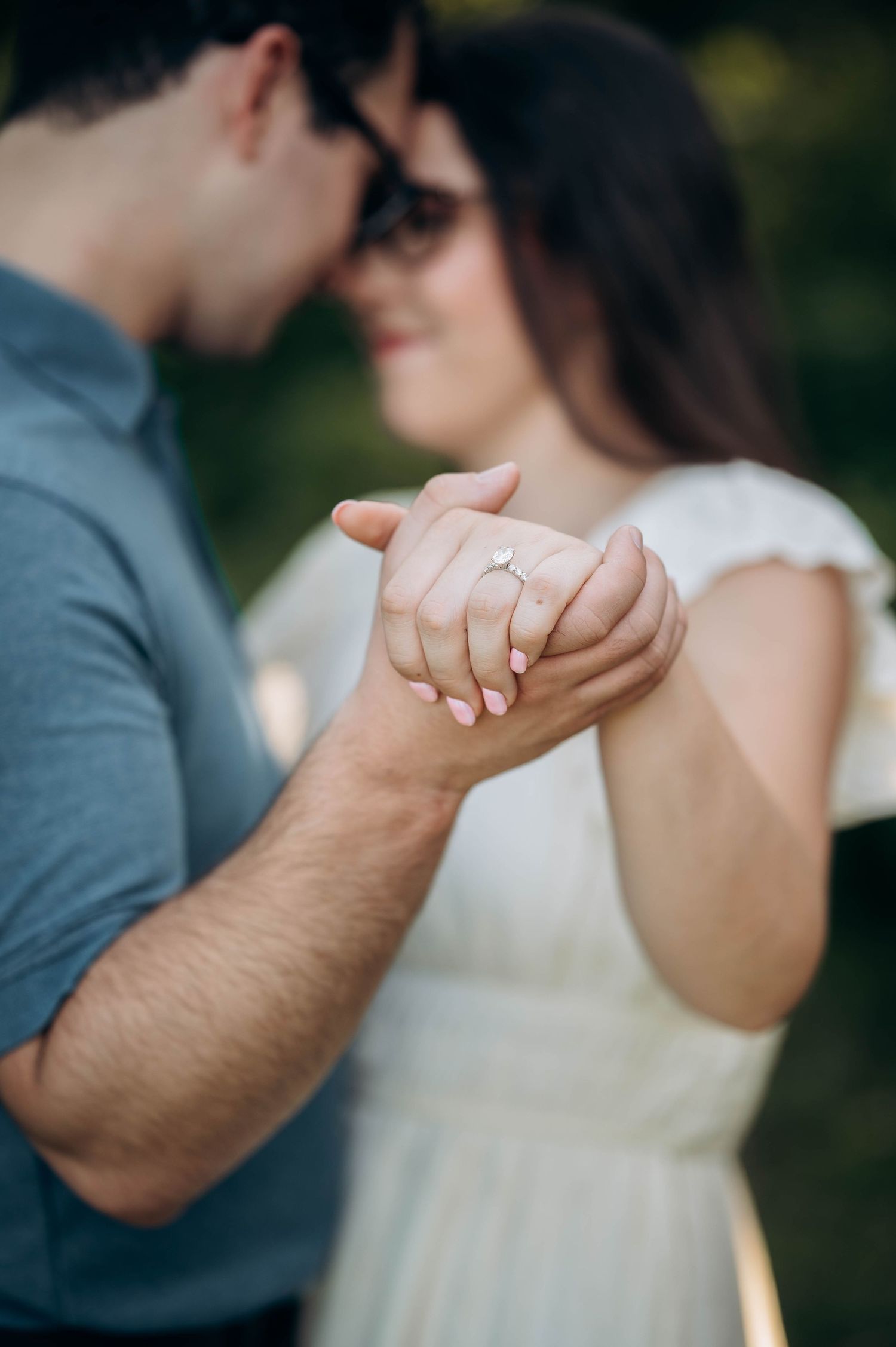 Close-up of intertwined hands showing engagement ring in soft natural lighting.