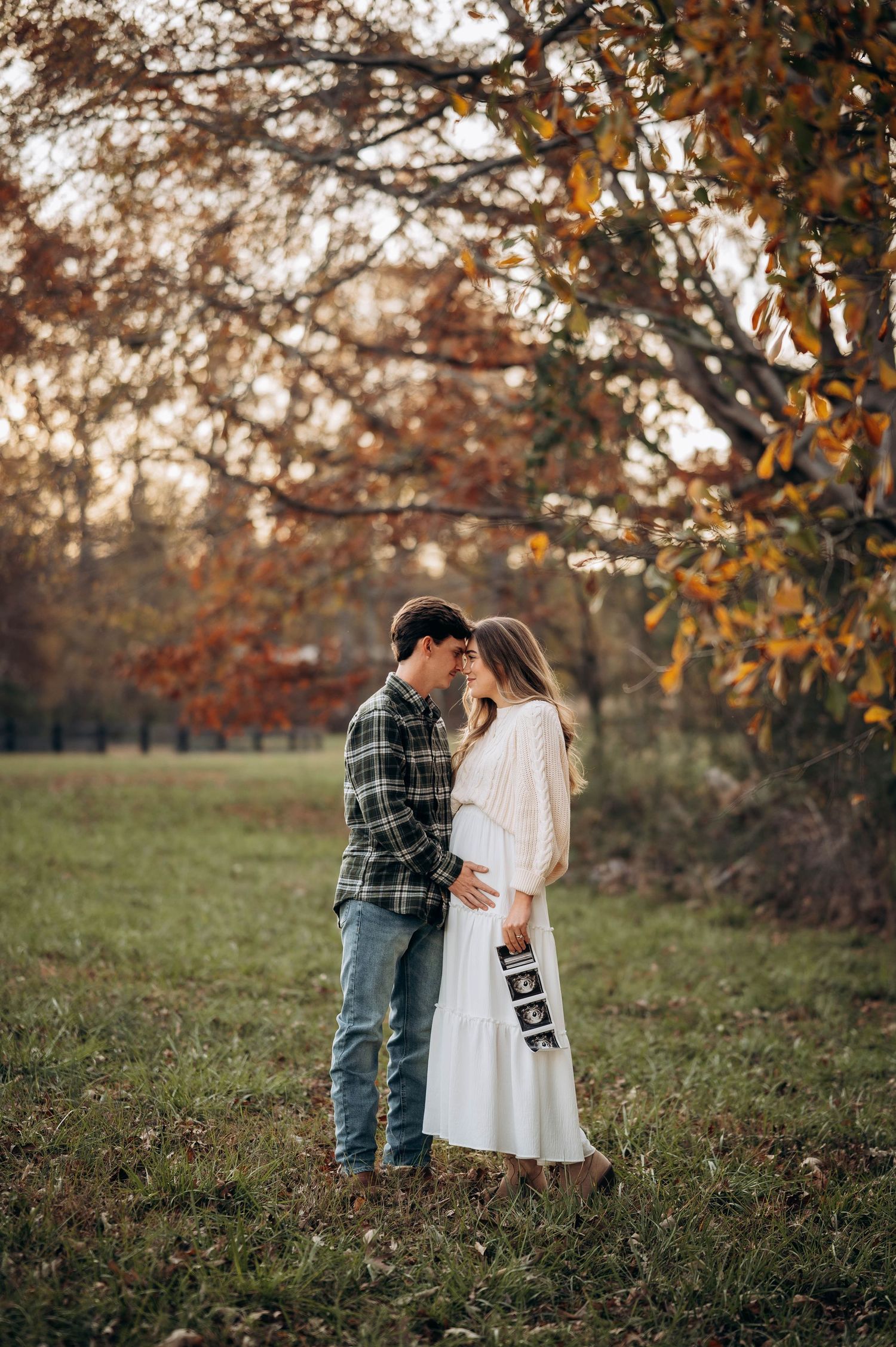 A romantic autumn photoshoot featuring a couple embracing in a field with fall foliage.