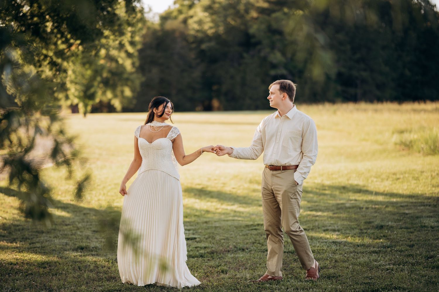 Bride and groom holding hands in a sunlit green field during an outdoor wedding photo session.