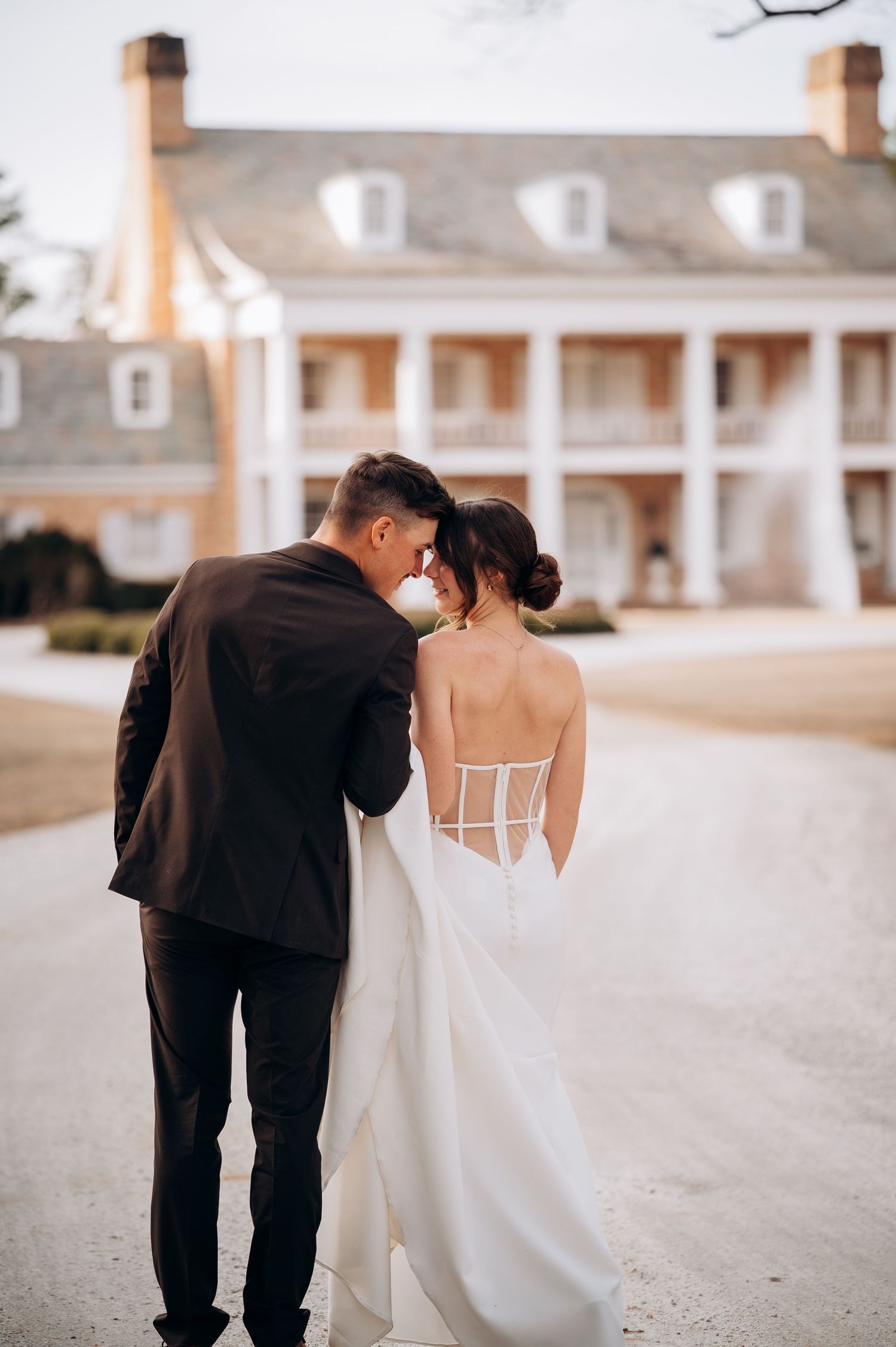 Bride and groom walk toward a grand Southern colonial mansion with white columns on their wedding day.